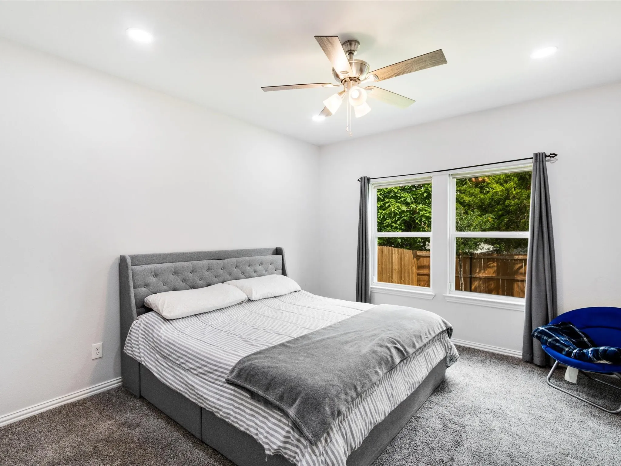 Bright bedroom featuring carpet flooring, a ceiling fan with integrated lighting, recessed overhead lighting, and two windows providing natural light