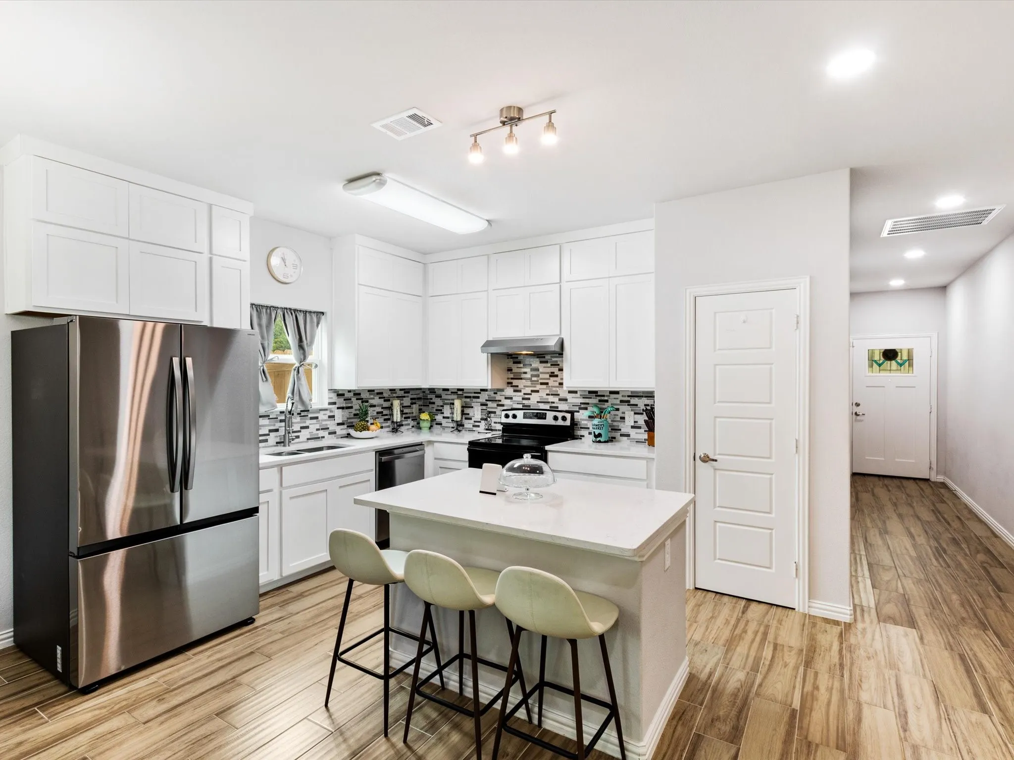 Bright kitchen featuring white cabinetry, a central island with countertop seating, stainless steel appliances, a mosaic tile backsplash, and wood-finish flooring