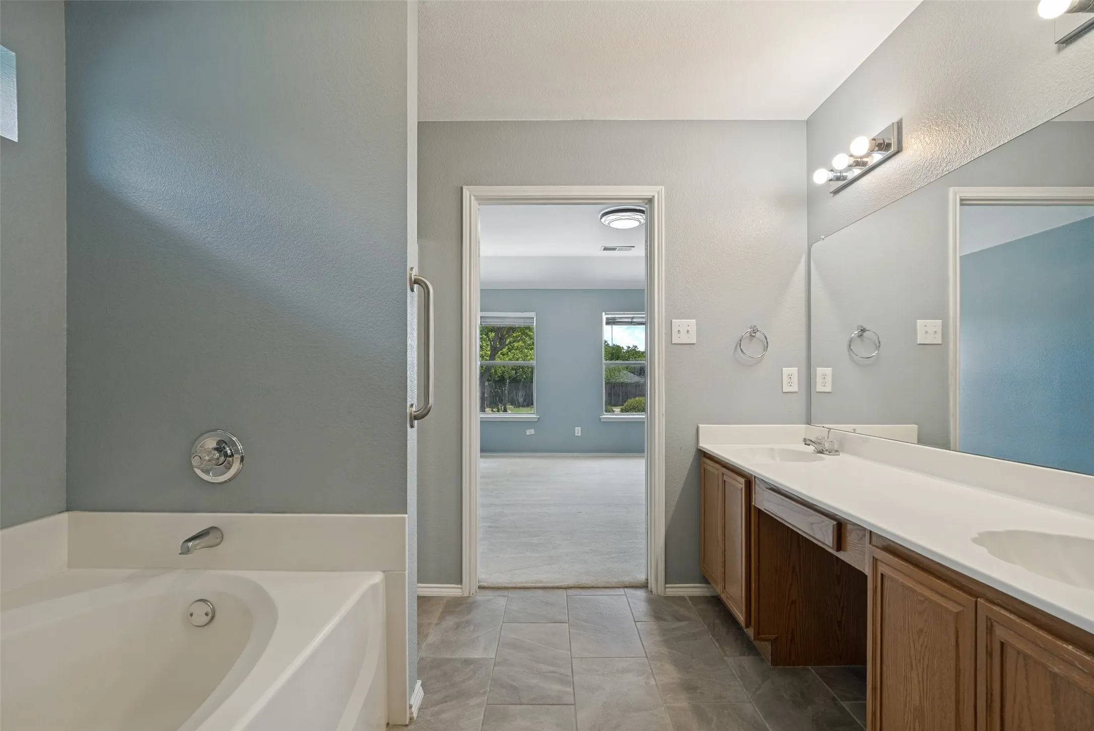 Bathroom featuring a built-in tub, dual sink vanity with wood cabinetry, and a full-width mirror