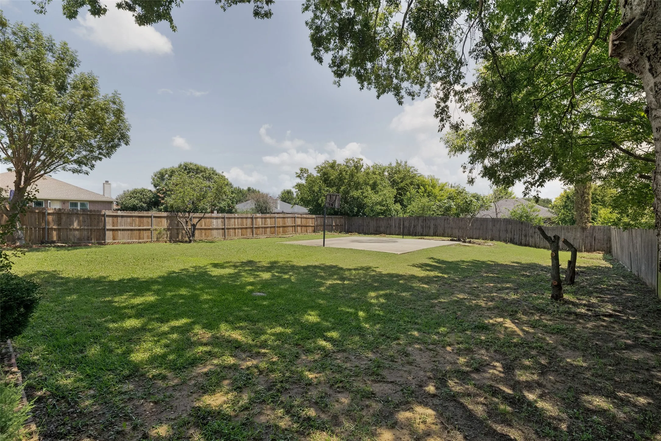 Expansive backyard featuring a large concrete pad, mature trees, and a full privacy fence