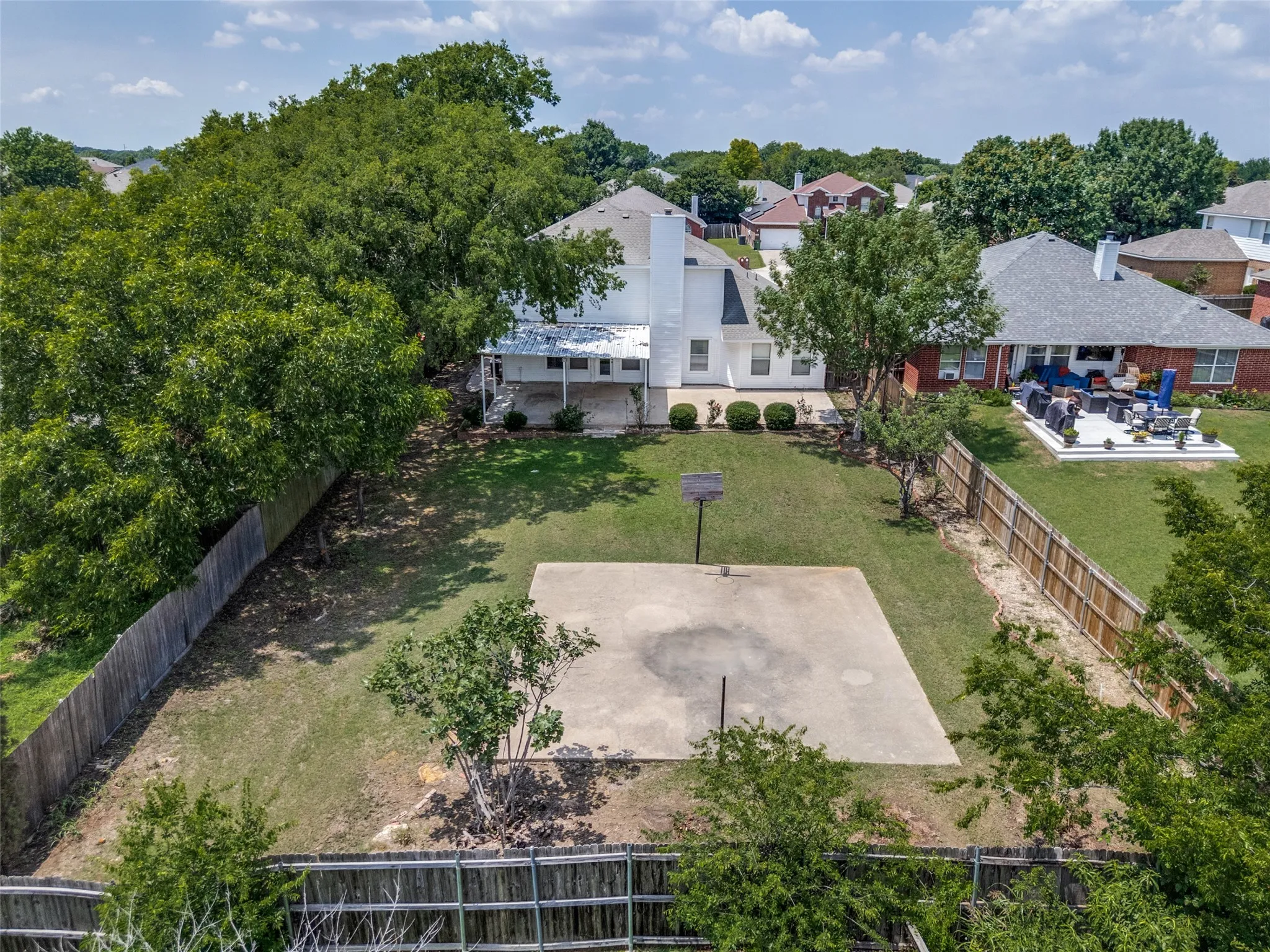 Expansive backyard featuring a large concrete pad, mature trees, and a wood fence enclosure