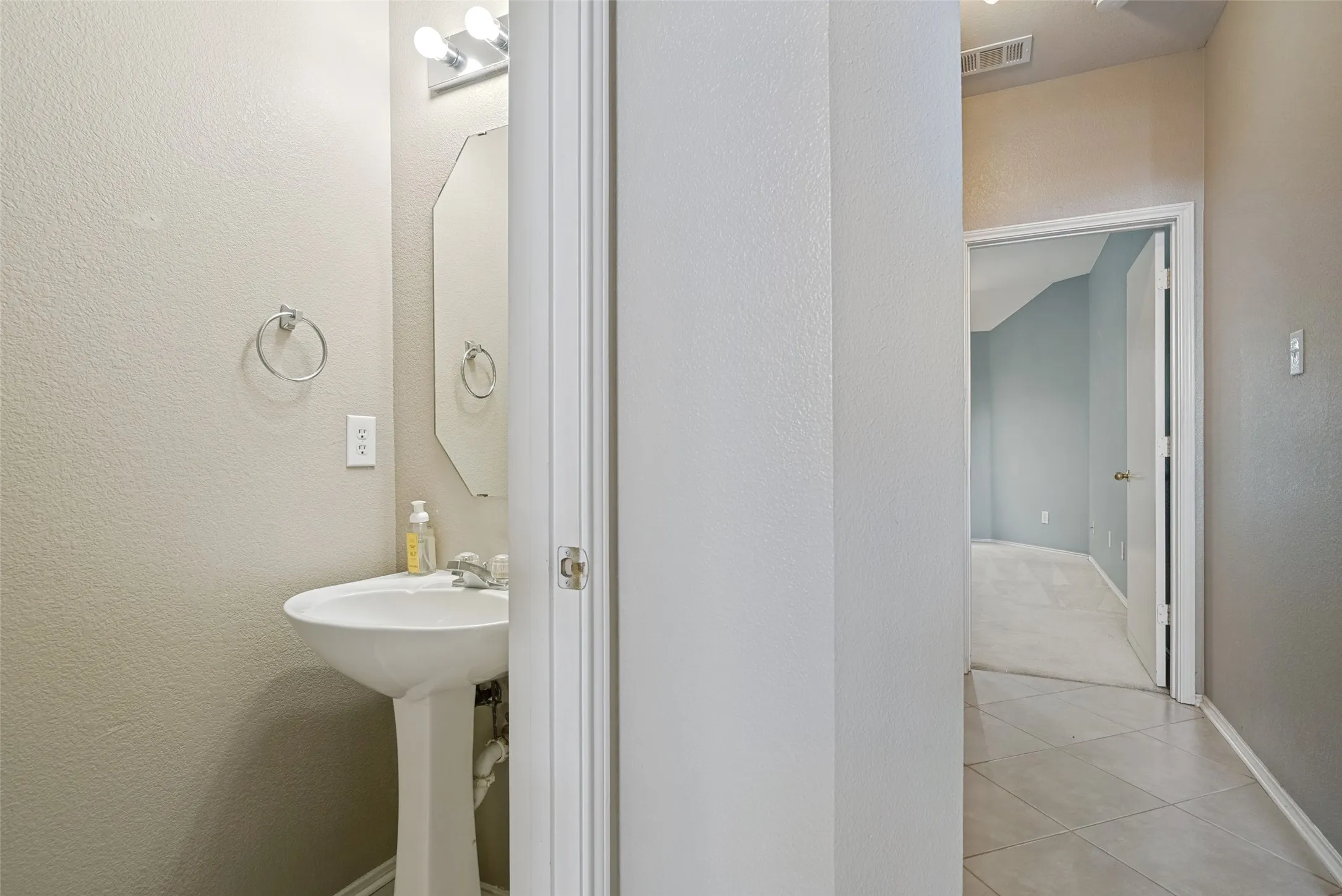 Pedestal sink with chrome fixtures, an octagonal wall mirror, and vanity lighting