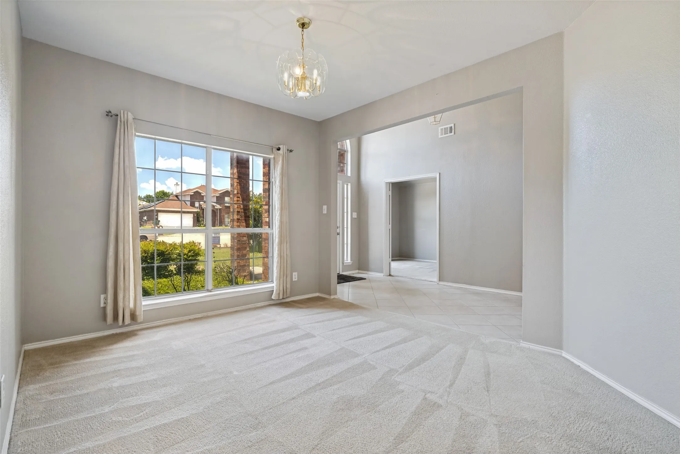 Carpeted interior space featuring a large multipane window, a contemporary chandelier, light-toned walls, and an arched entry