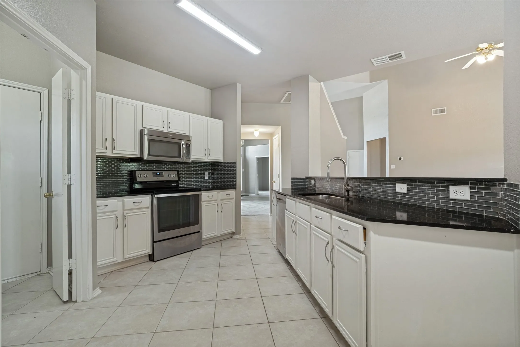 Kitchen featuring white cabinetry, stainless steel appliances, dark countertops, a dark tile backsplash, and tile flooring