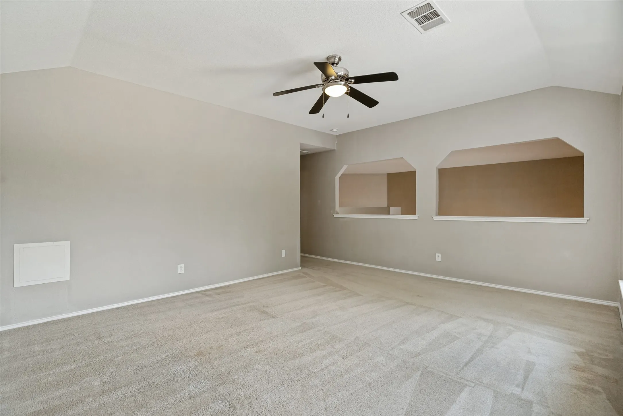 Spacious interior room featuring vaulted ceilings, light gray wall paint, and plush carpet flooring