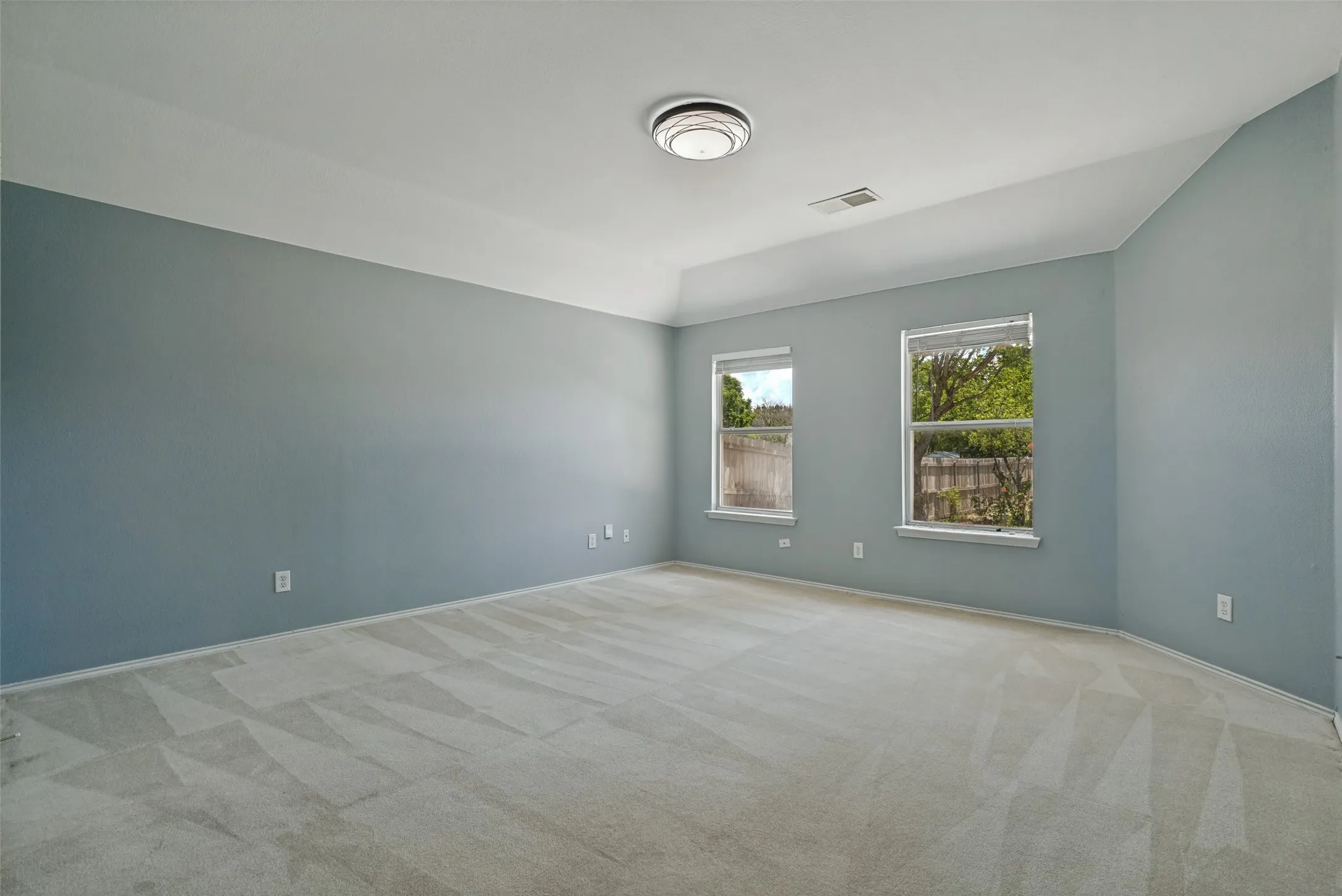 Spacious room featuring light blue walls, two windows, vaulted ceiling, and carpet flooring