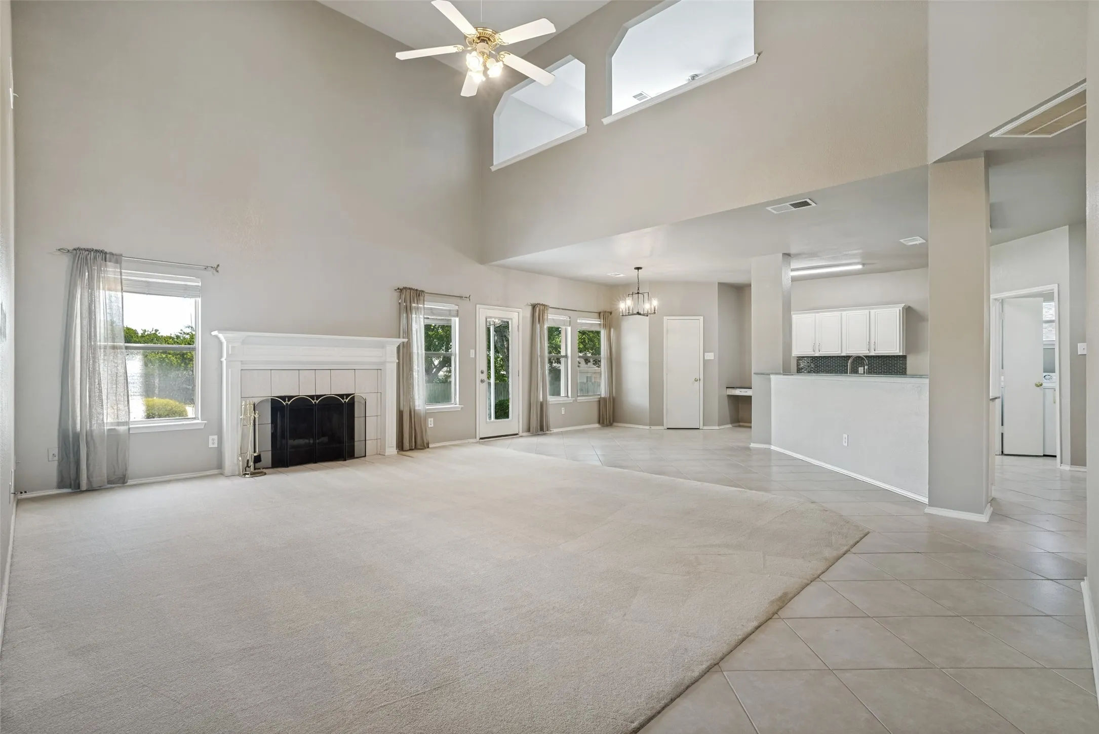 Spacious living area featuring a vaulted ceiling with a ceiling fan, a fireplace with a decorative mantel, multiple windows, and a combination of carpet and tile flooring