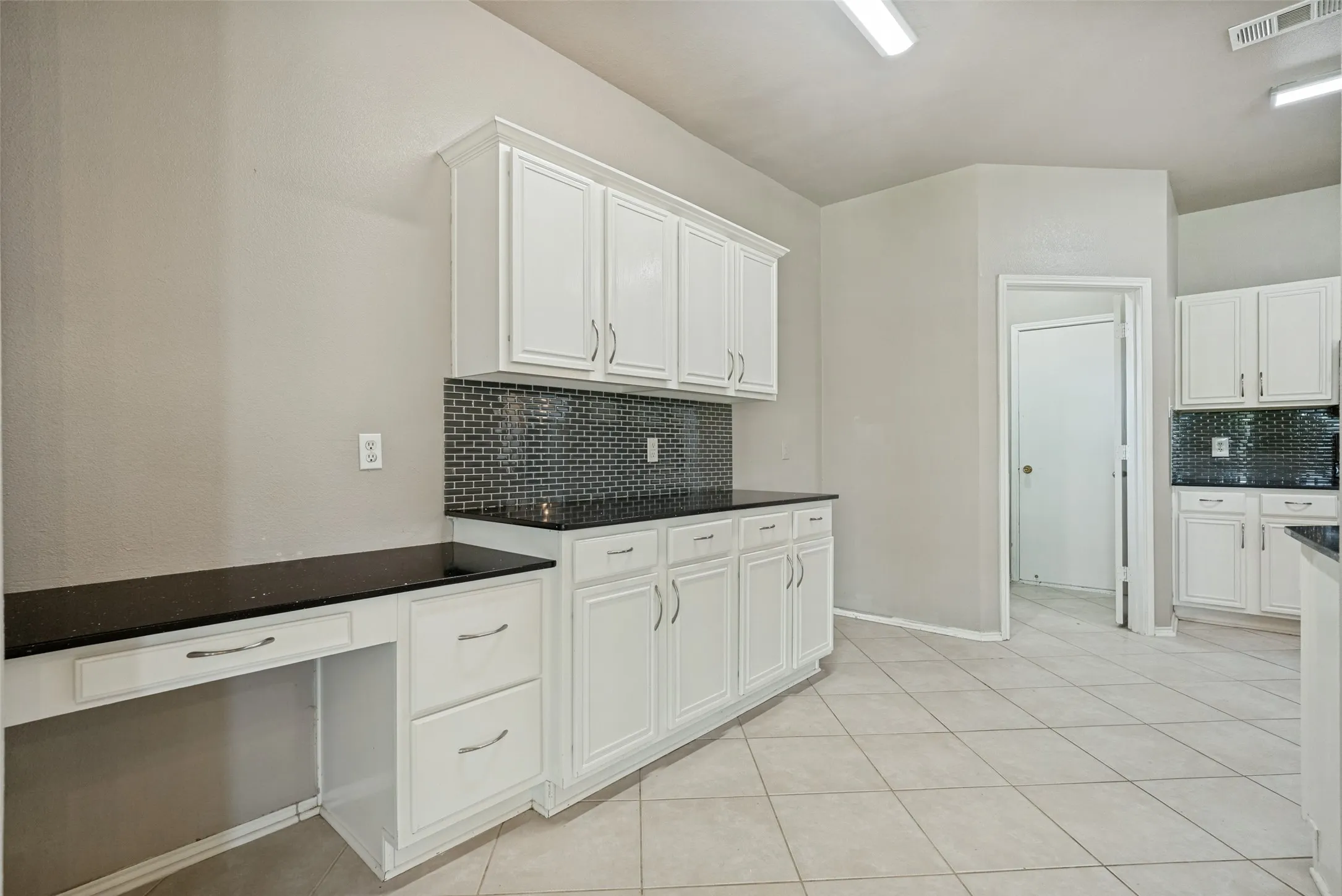 White cabinetry with brushed nickel hardware, dark countertops, and a full-height dark tile backsplash