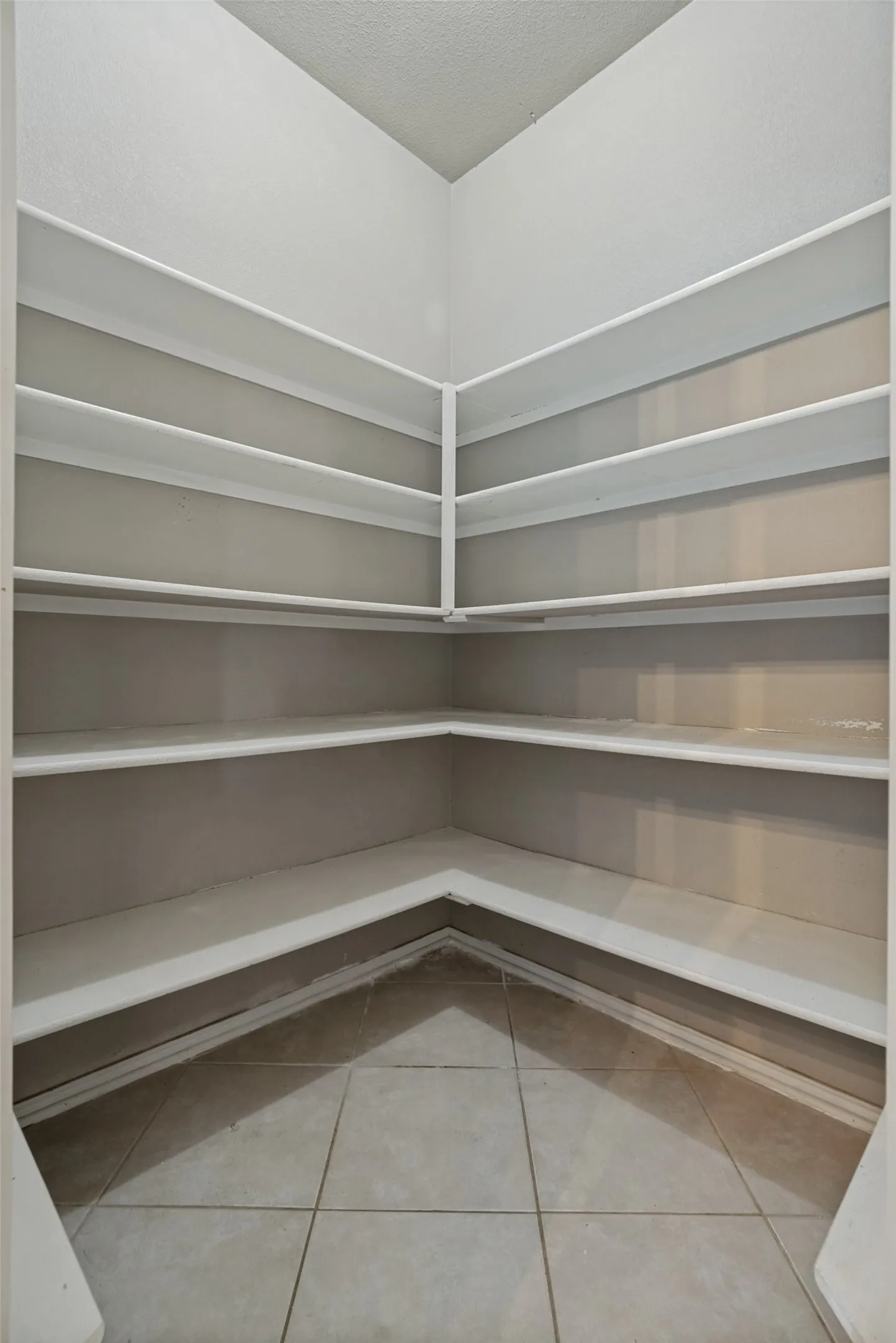 Built-in pantry shelving featuring multiple tiers, light gray wall paint, white trim, and square tile flooring