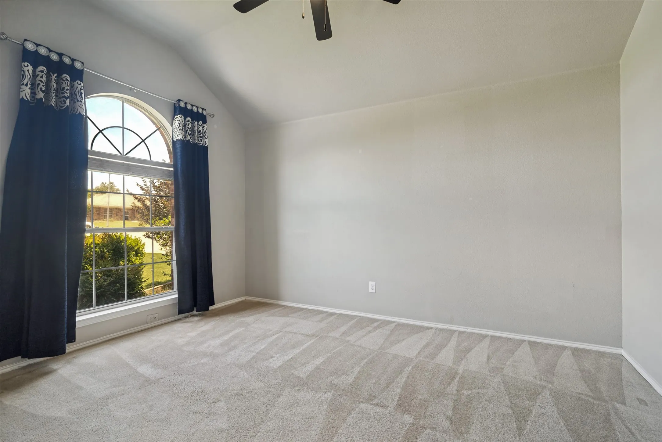 Spacious room featuring vaulted ceilings, a large arched window, neutral wall tones, and patterned carpet flooring