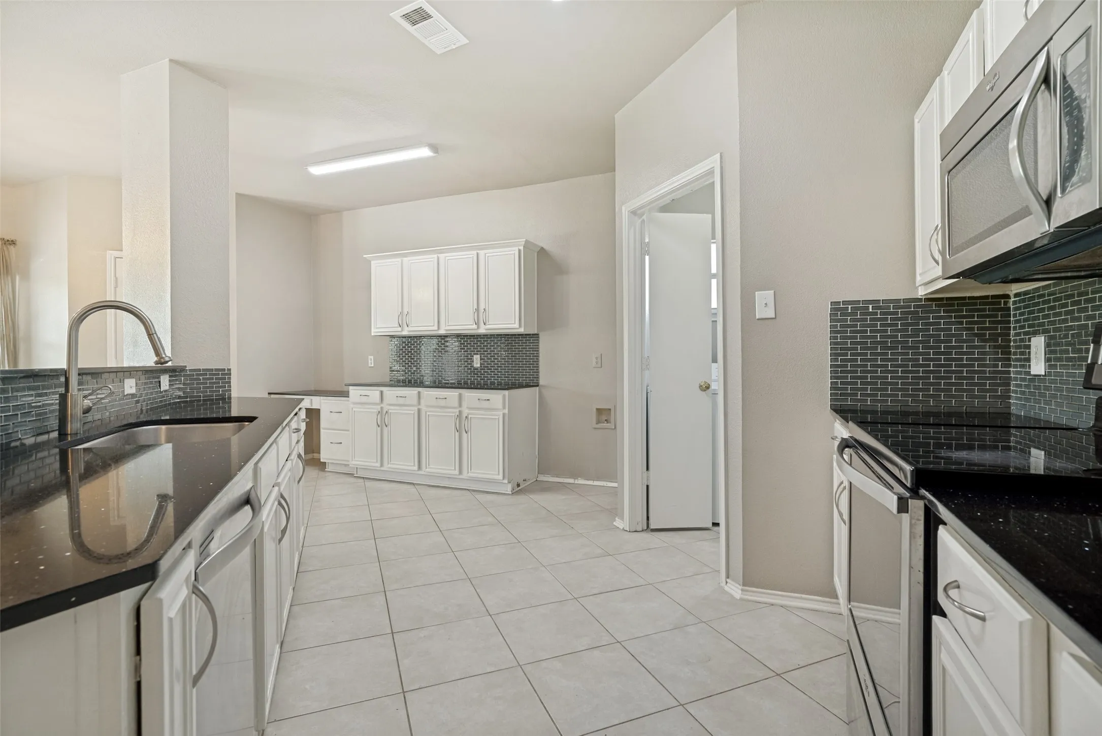 Kitchen featuring white cabinetry, dark speckled countertops, and a gray tile backsplash