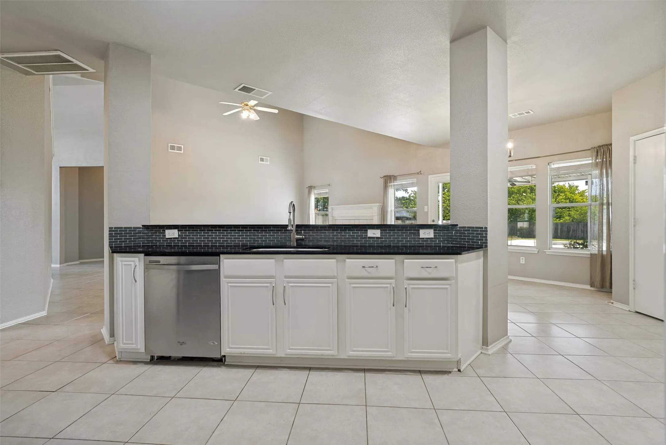 Kitchen island featuring white cabinetry, black countertops, a stainless steel dishwasher, and a dark tile backsplash