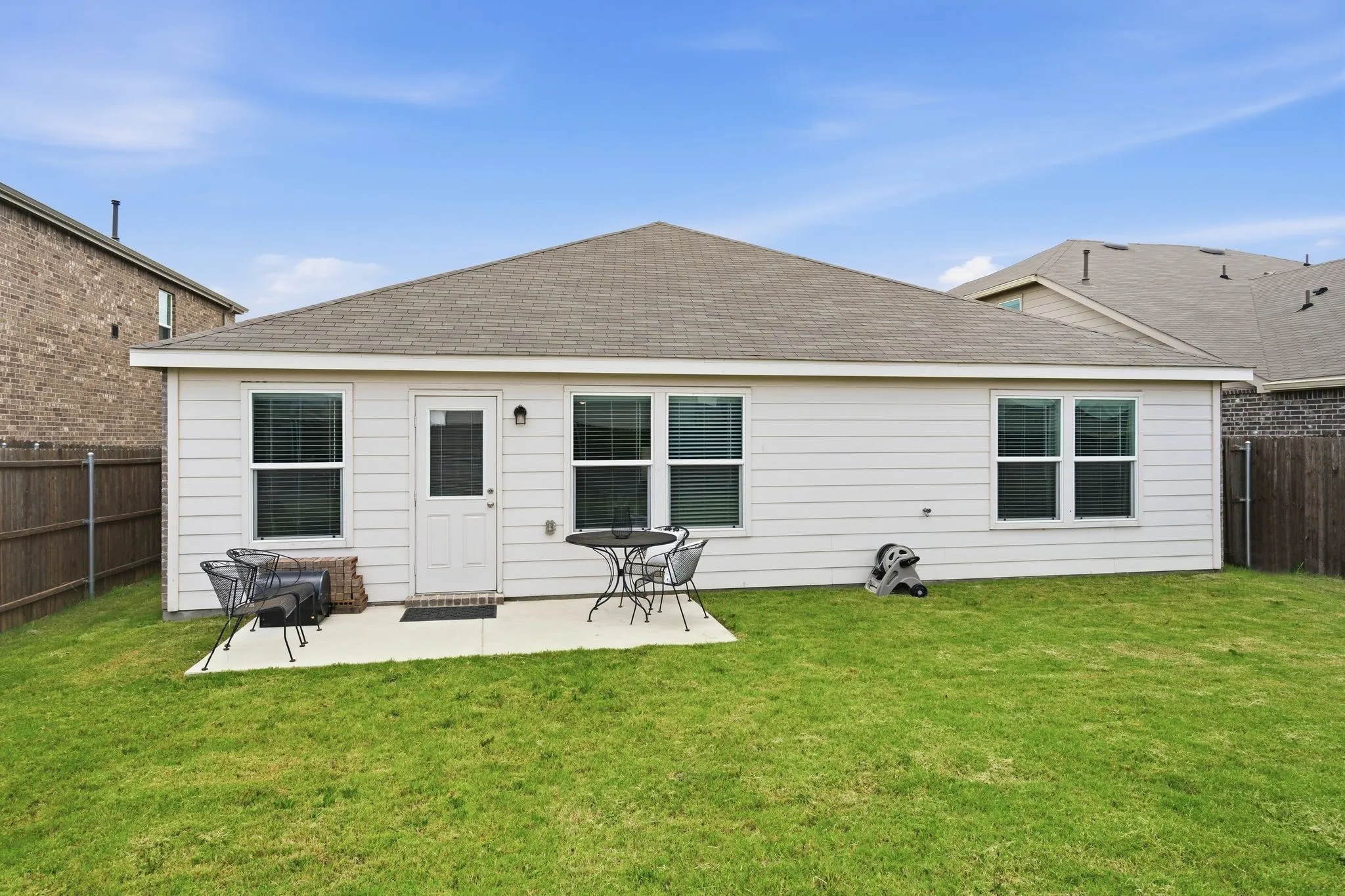 Expansive backyard featuring a manicured lawn, concrete patio, and a white paneled exterior with multiple windows
