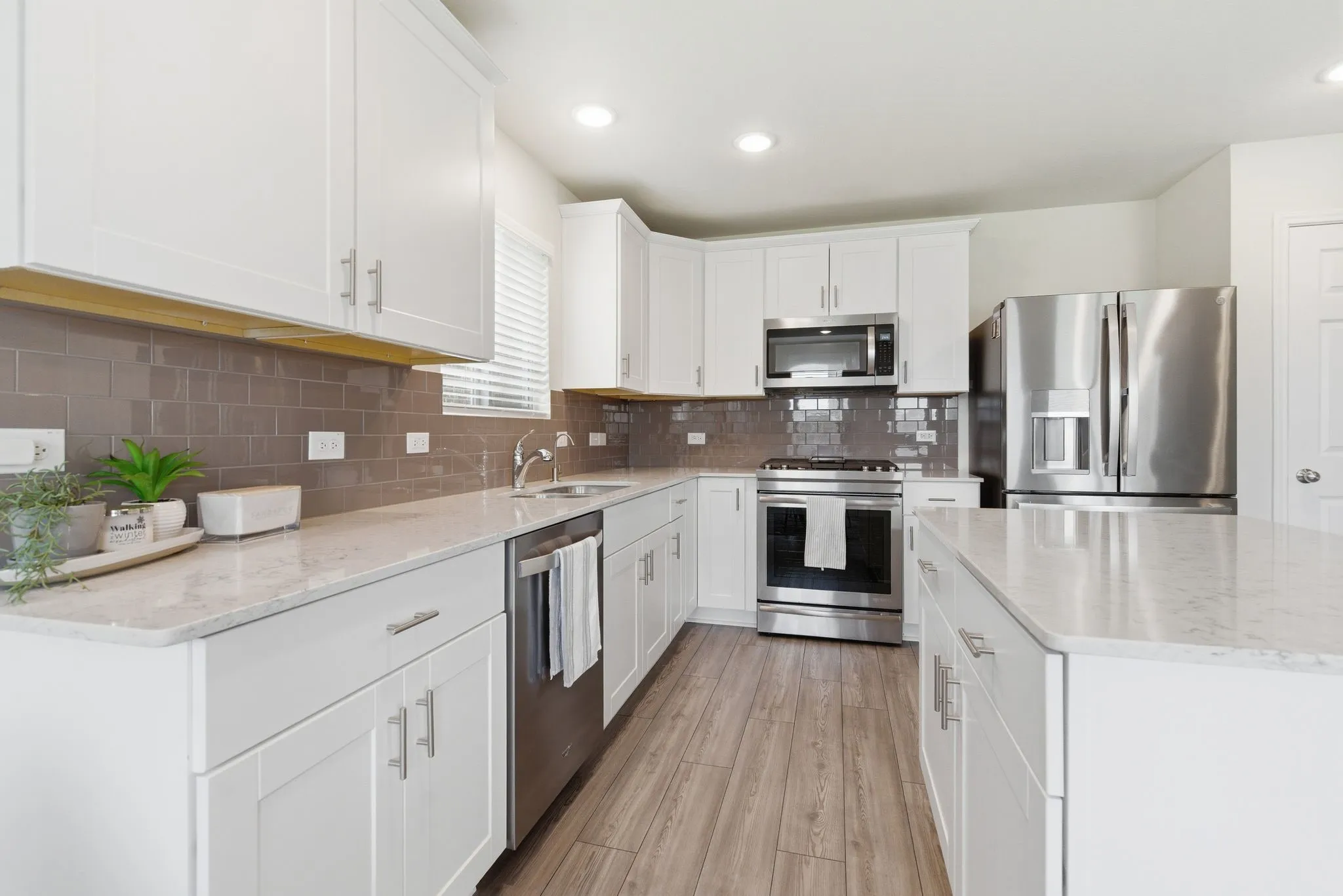 Contemporary kitchen with white shaker cabinetry, stainless steel appliances, light-toned silestone quartz countertops, a subway tile backsplash, and wood-look tile flooring
