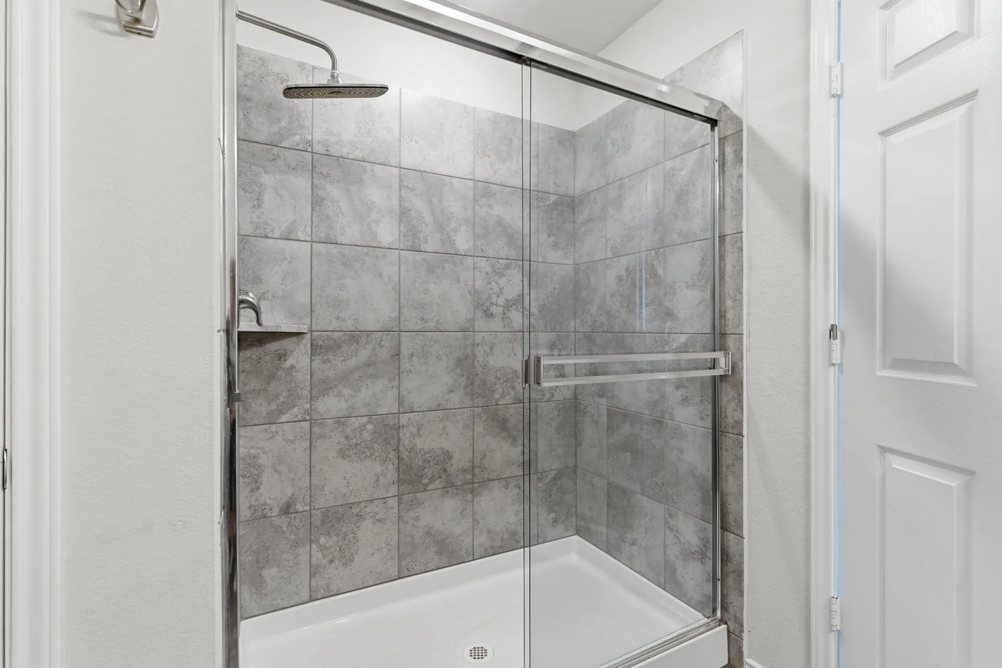 Shower enclosure featuring a sliding glass door, gray tile surround, rainfall showerhead, and a built-in shower niche