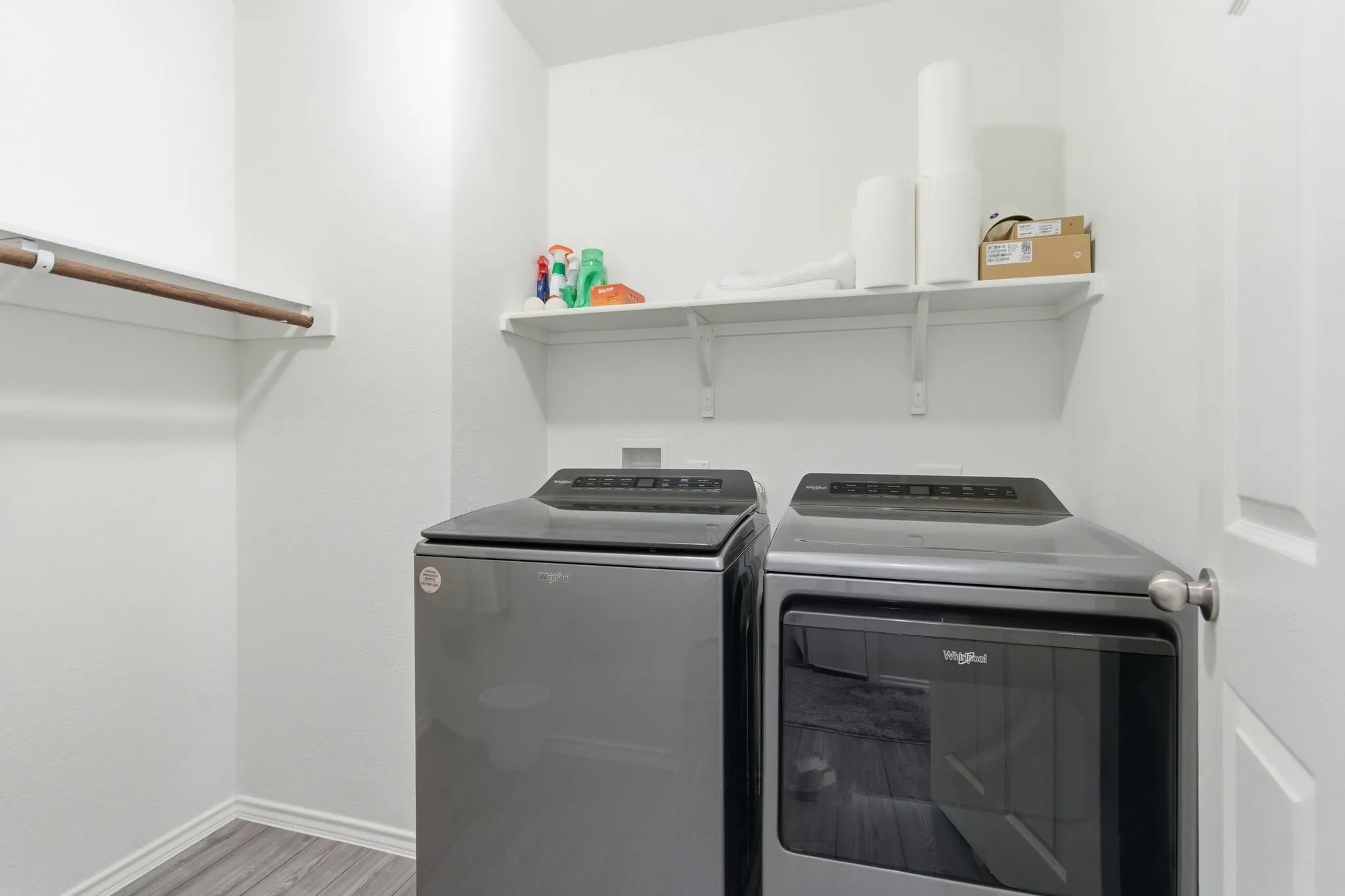 Dedicated laundry area featuring wood-look tile flooring, a wall-mounted shelving unit, and a clothes hanging rod