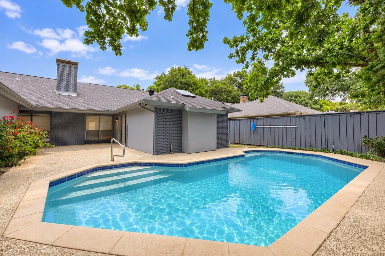 Private backyard featuring an in-ground swimming pool with integrated steps, surrounding concrete patio, and a privacy fence