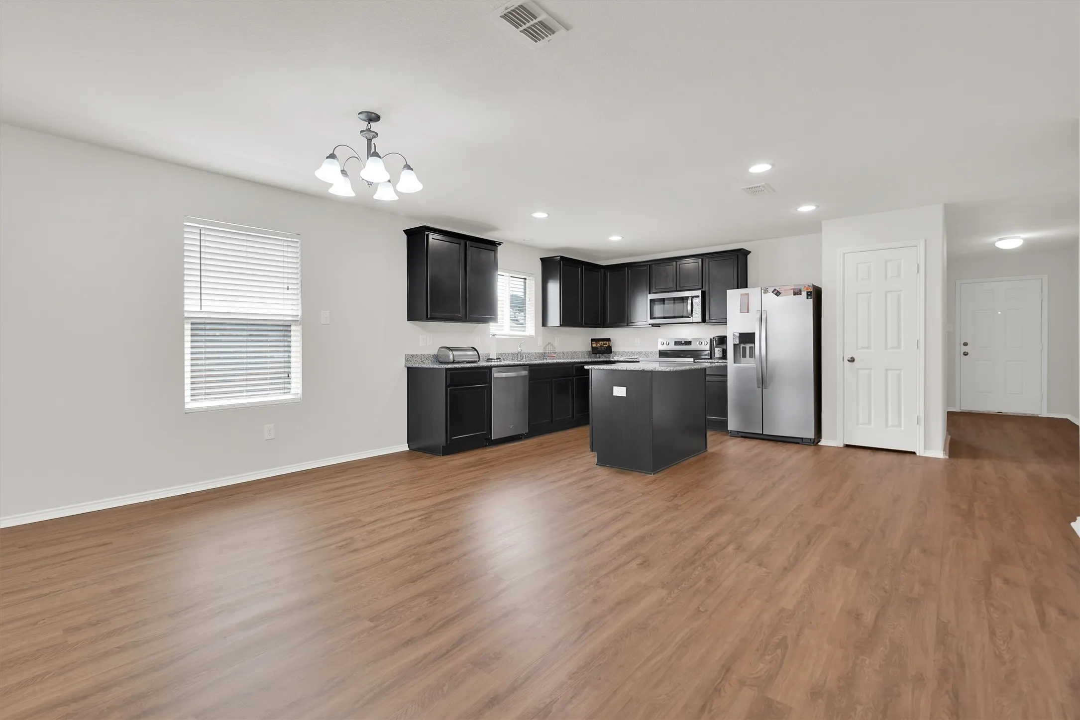 Open-concept living area featuring wood-finish flooring, a kitchen island, dark cabinetry, and recessed lighting