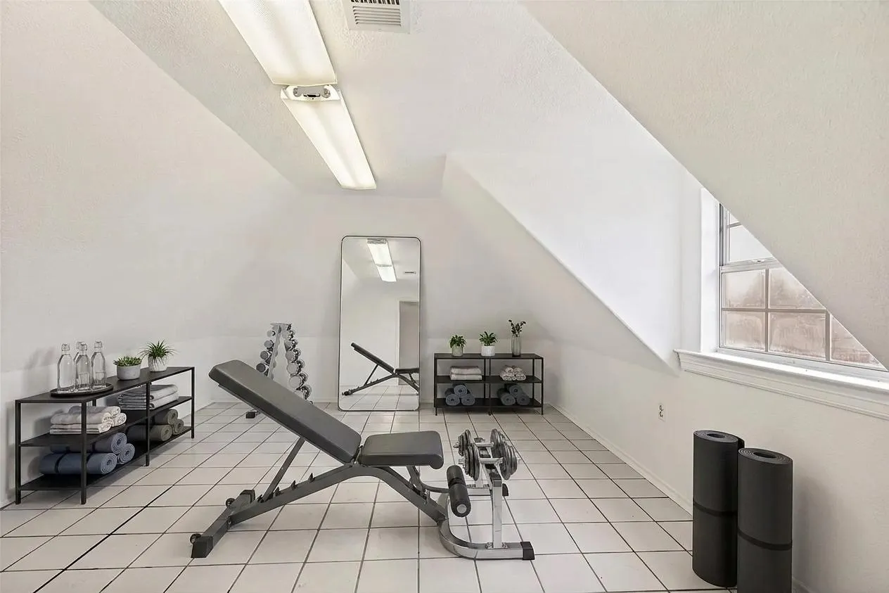 Sloping ceiling lines with track lighting, white tiled flooring, and a glass block window
