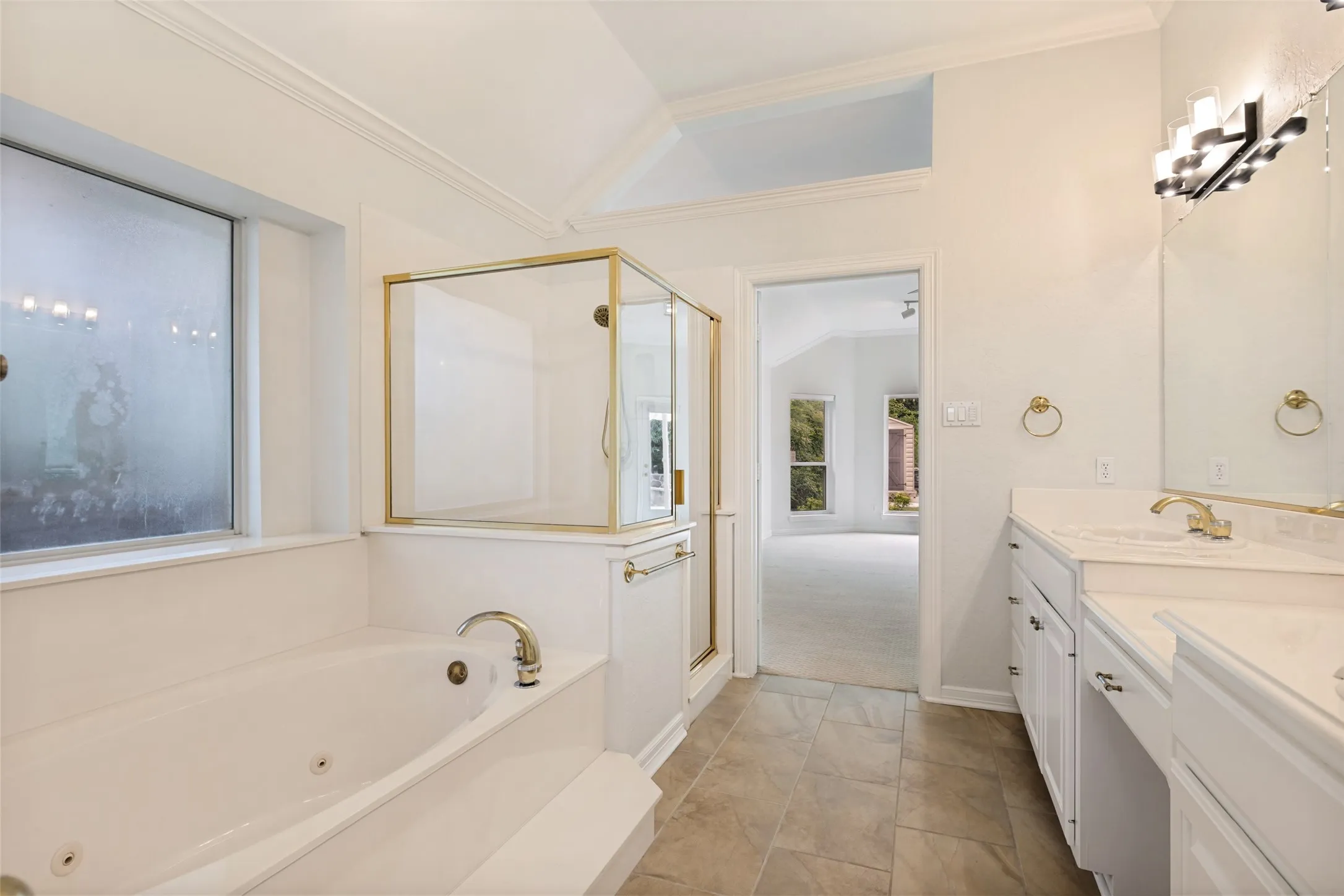 Bathroom featuring a built-in jetted tub, a separate glass-enclosed shower with brass-tone framing, dual vanity with solid surface countertops, and tile flooring