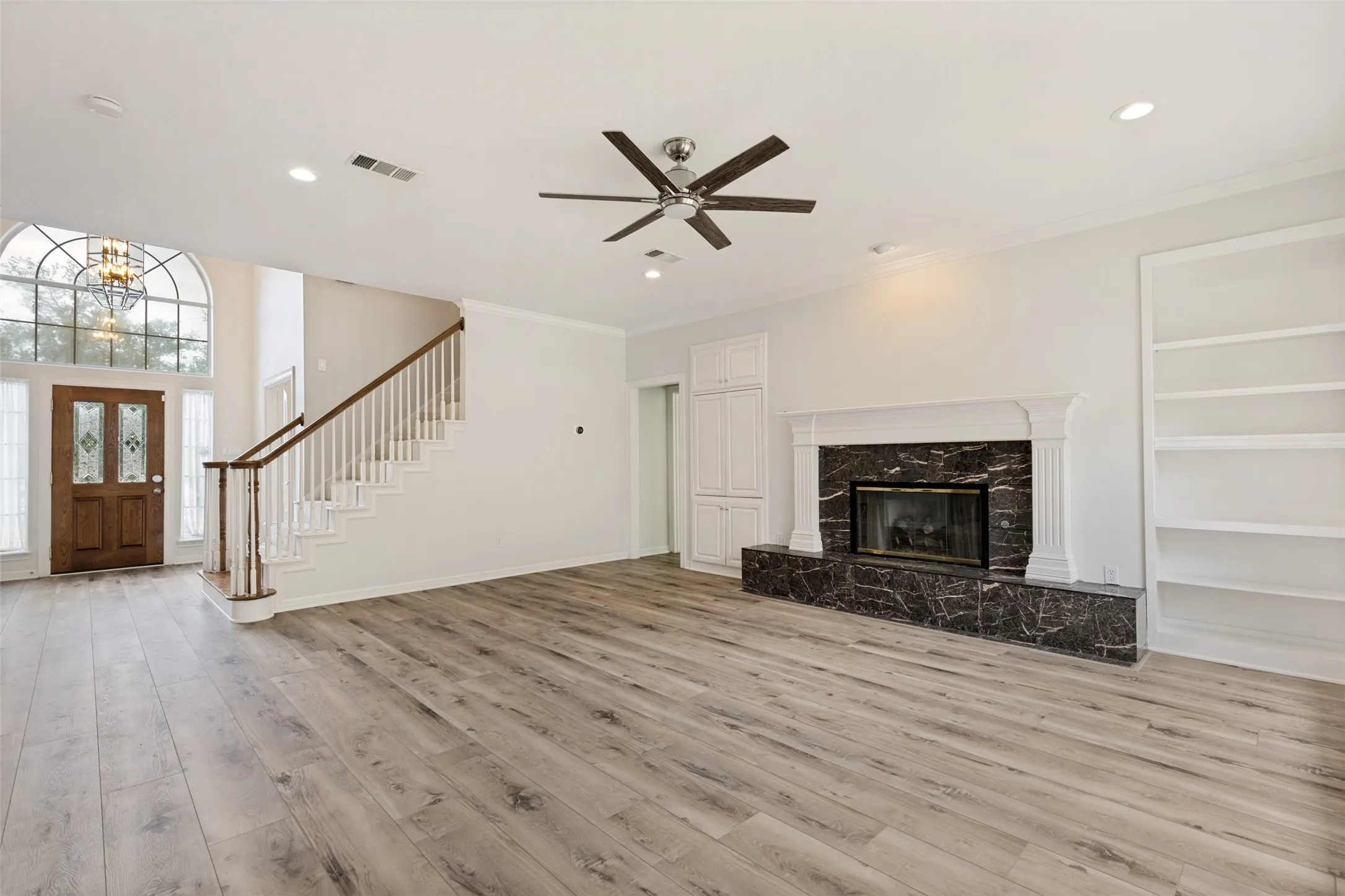 Spacious living area featuring wood-finish flooring, a decorative fireplace with a marble surround, and built-in shelving