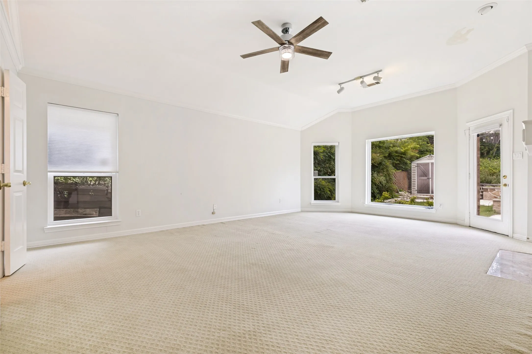 Spacious room featuring vaulted ceilings, crown molding, and neutral carpet flooring