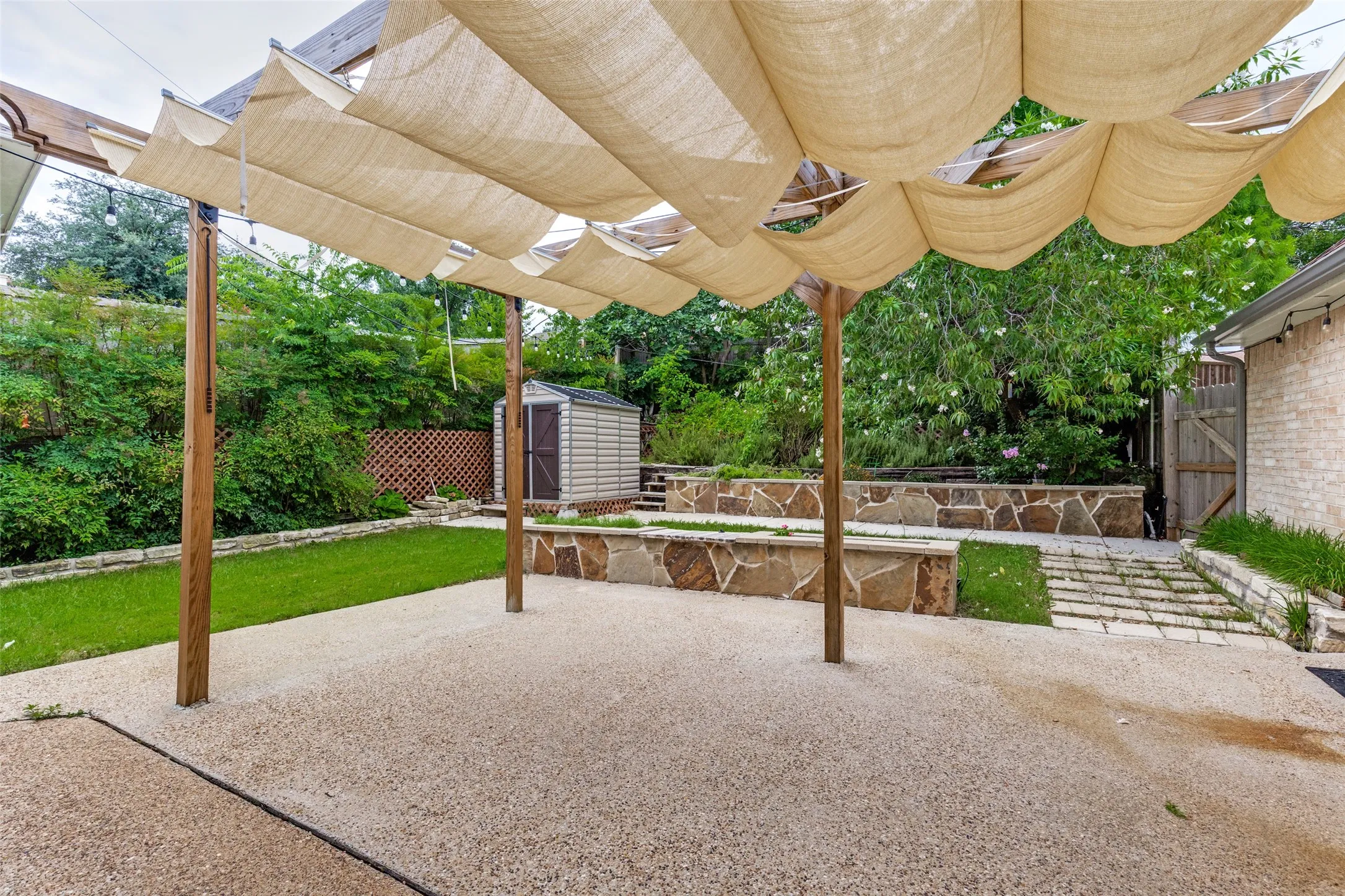 Expansive outdoor patio area featuring a light-colored aggregate surface under a wood pergola with retractable fabric shades