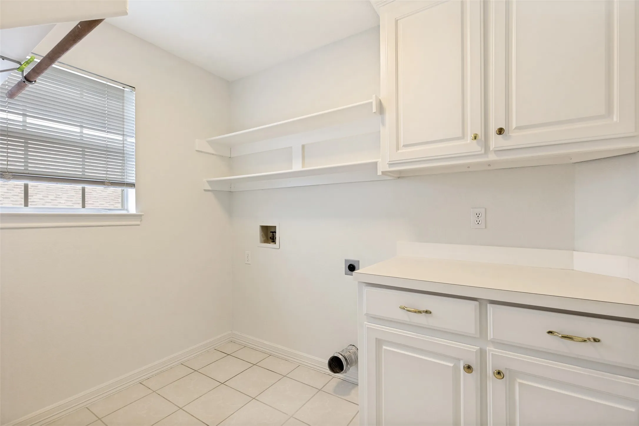 Laundry room featuring white cabinetry, a countertop surface, open shelving, and a window with blinds