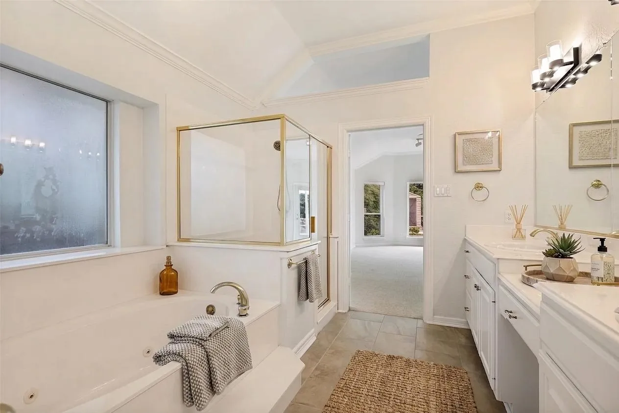 Primary Bathroom featuring a freestanding soaking tub with brushed nickel fixtures, a walk-in shower with frameless glass enclosure, dual vanity with white cabinetry and integrated sink, quartz countertop, polished chrome hardware, recessed lighting, and natural light from a window