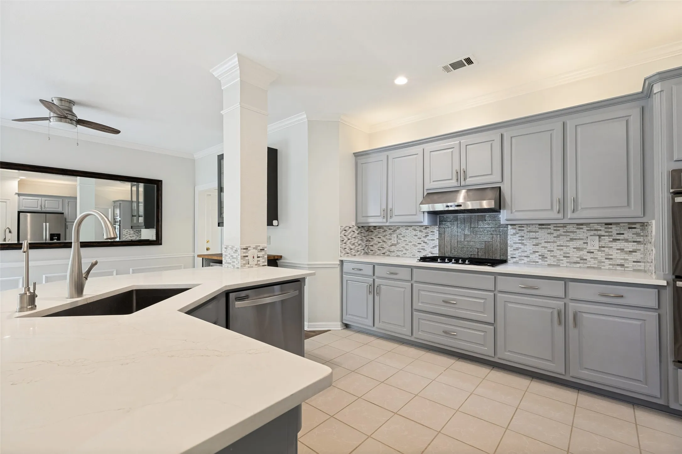 Kitchen featuring an expansive island with an undermount sink, quartz countertops, gray cabinetry, a mosaic tile backsplash, and stainless steel appliances
