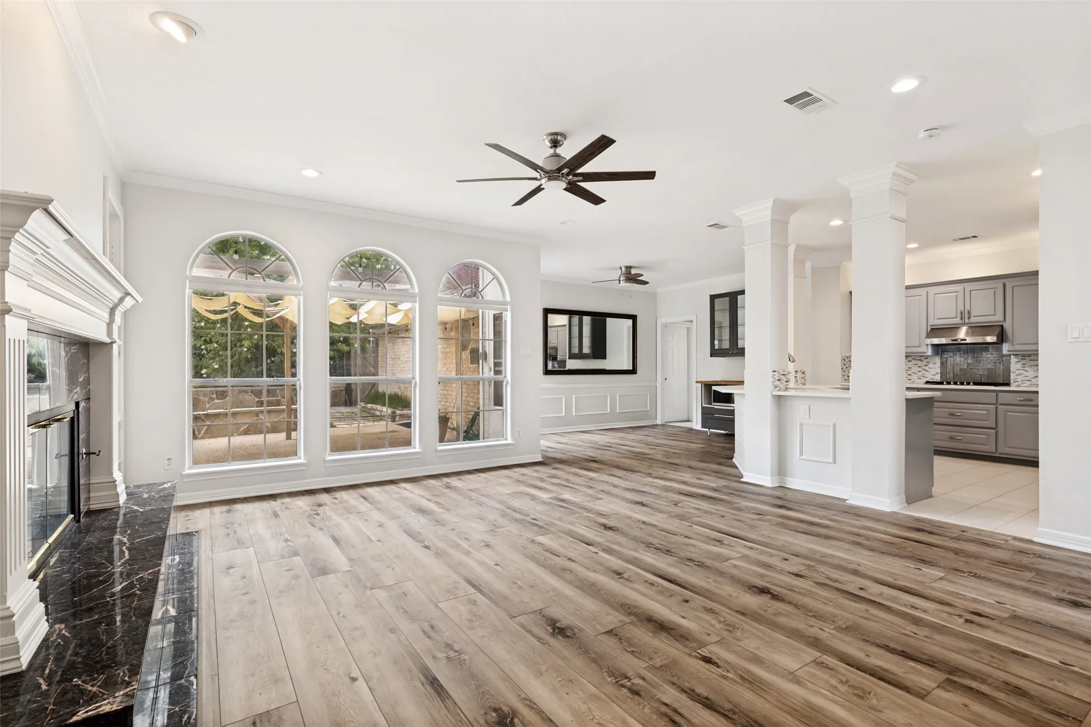 Spacious living area featuring wood-finish flooring, a decorative fireplace with a dark marble surround, and three arched windows