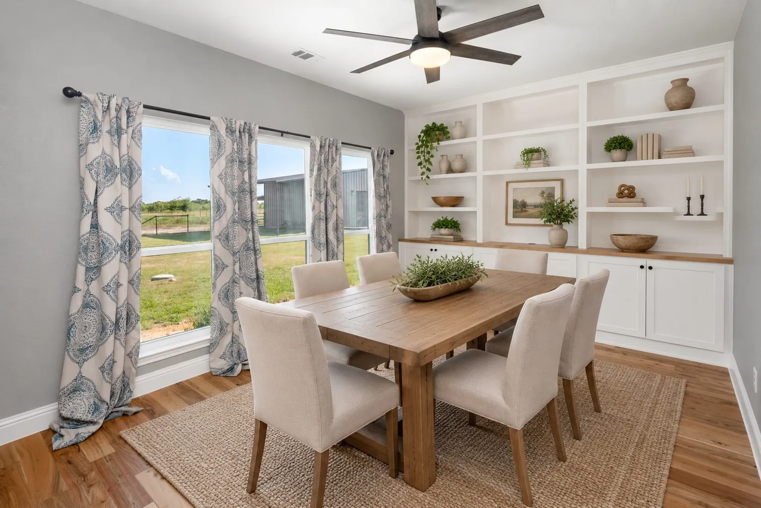 Built-in shelving with lower cabinetry and wood-finish countertops, wood-finish flooring, a ceiling fan with integrated lighting, and multiple windows