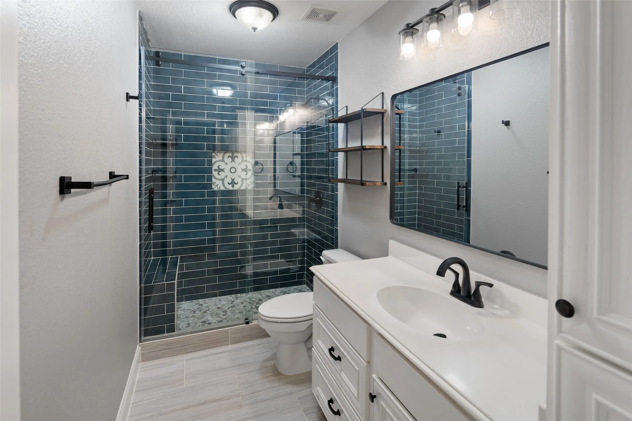 Bathroom featuring a glass-enclosed shower with dark teal subway tile, a decorative accent tile, and a pebble-style shower floor
