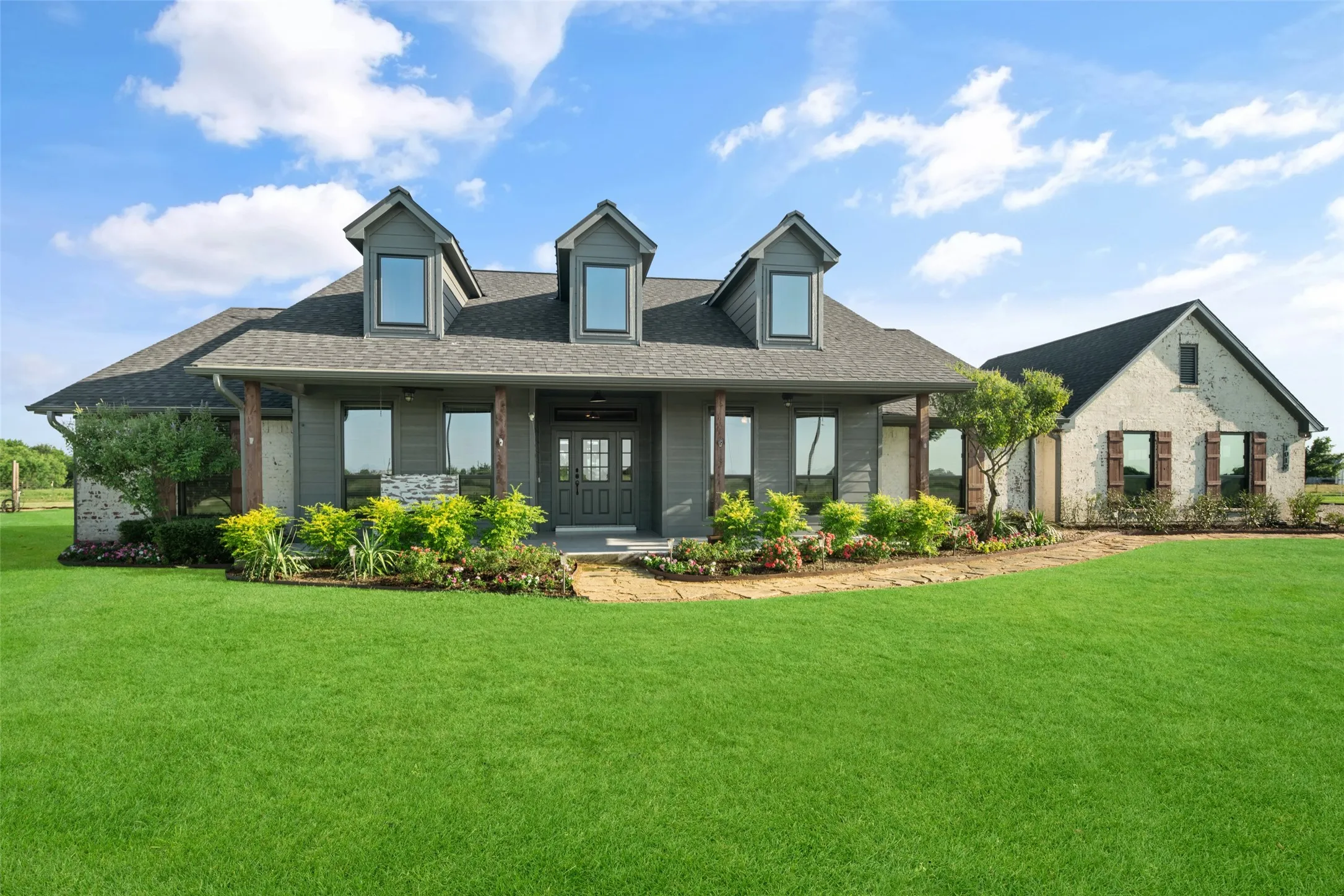 Ranch-style residence featuring a prominent front porch with wood-finish columns, a dark gray façade, and multiple dormer windows