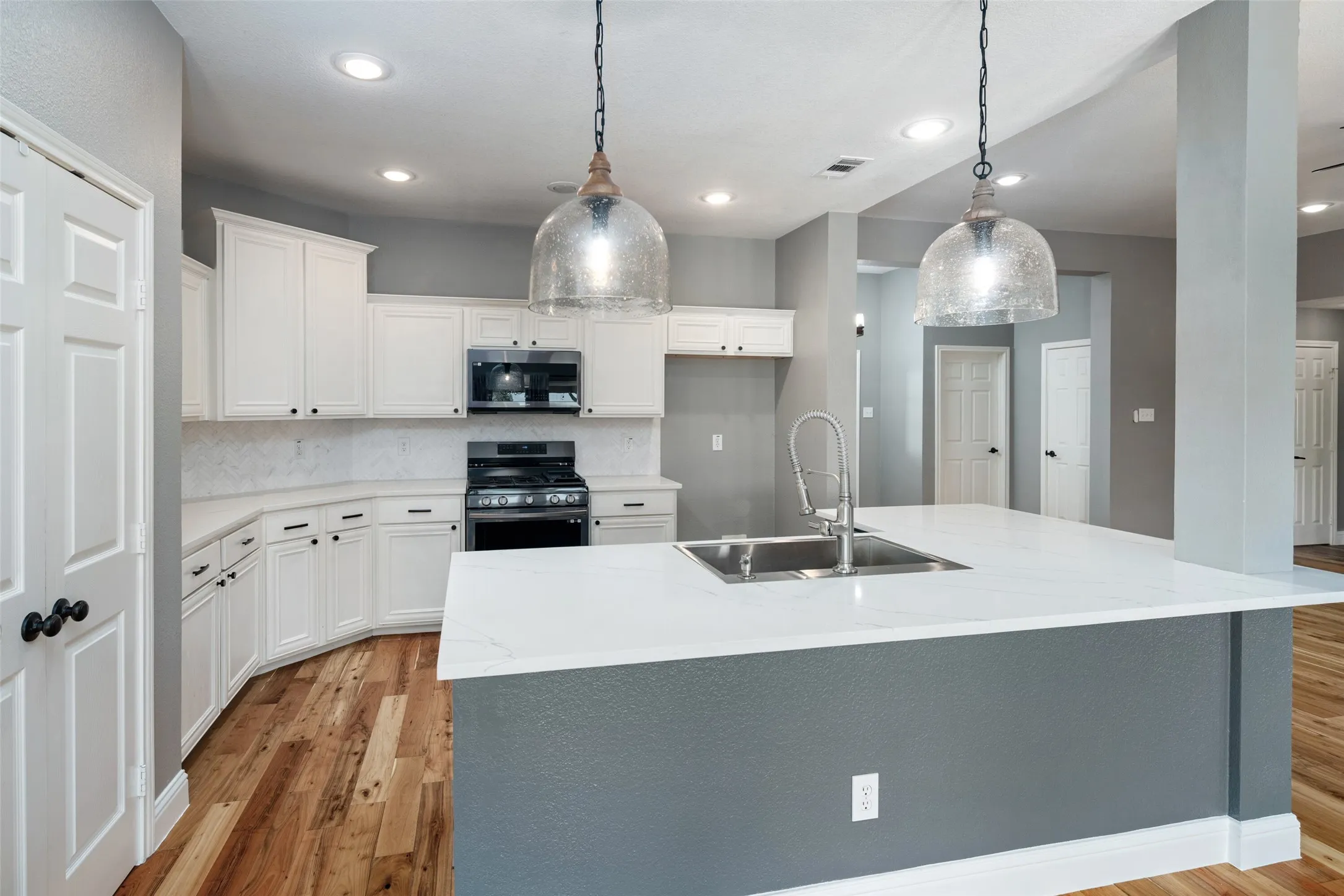 Kitchen featuring white cabinetry, wood-finish flooring, recessed lighting, and a kitchen island with a double basin sink and a high-arc faucet