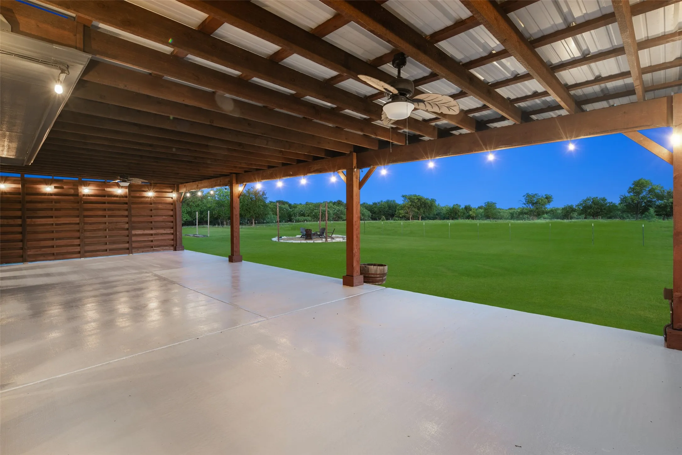 Expansive covered patio with a smooth concrete surface, wood beam ceiling, and string lighting