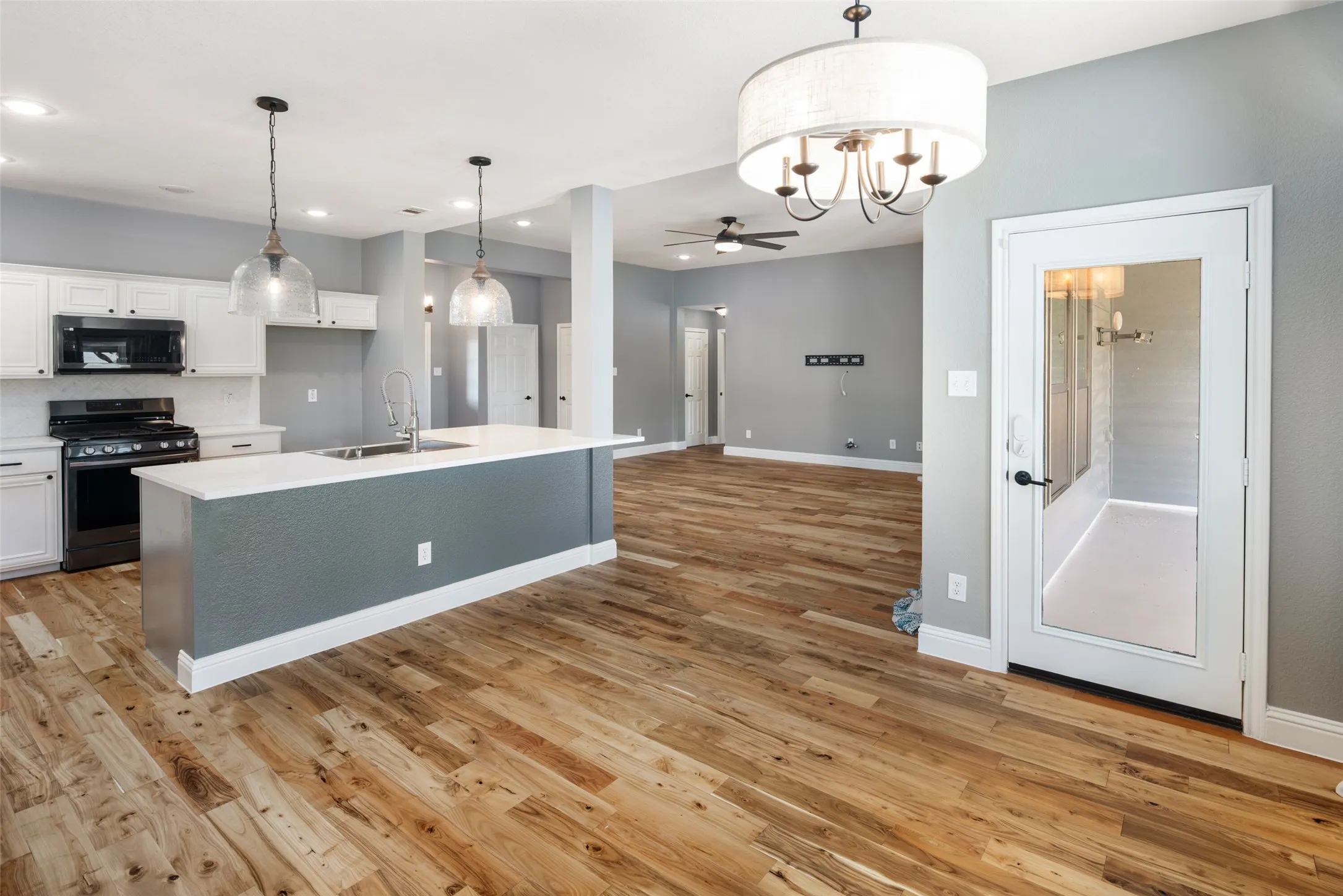 Open-concept living area featuring wood-finish flooring, a kitchen island with a sink and pendant lighting, white cabinetry, and a black range with an overhead microwave