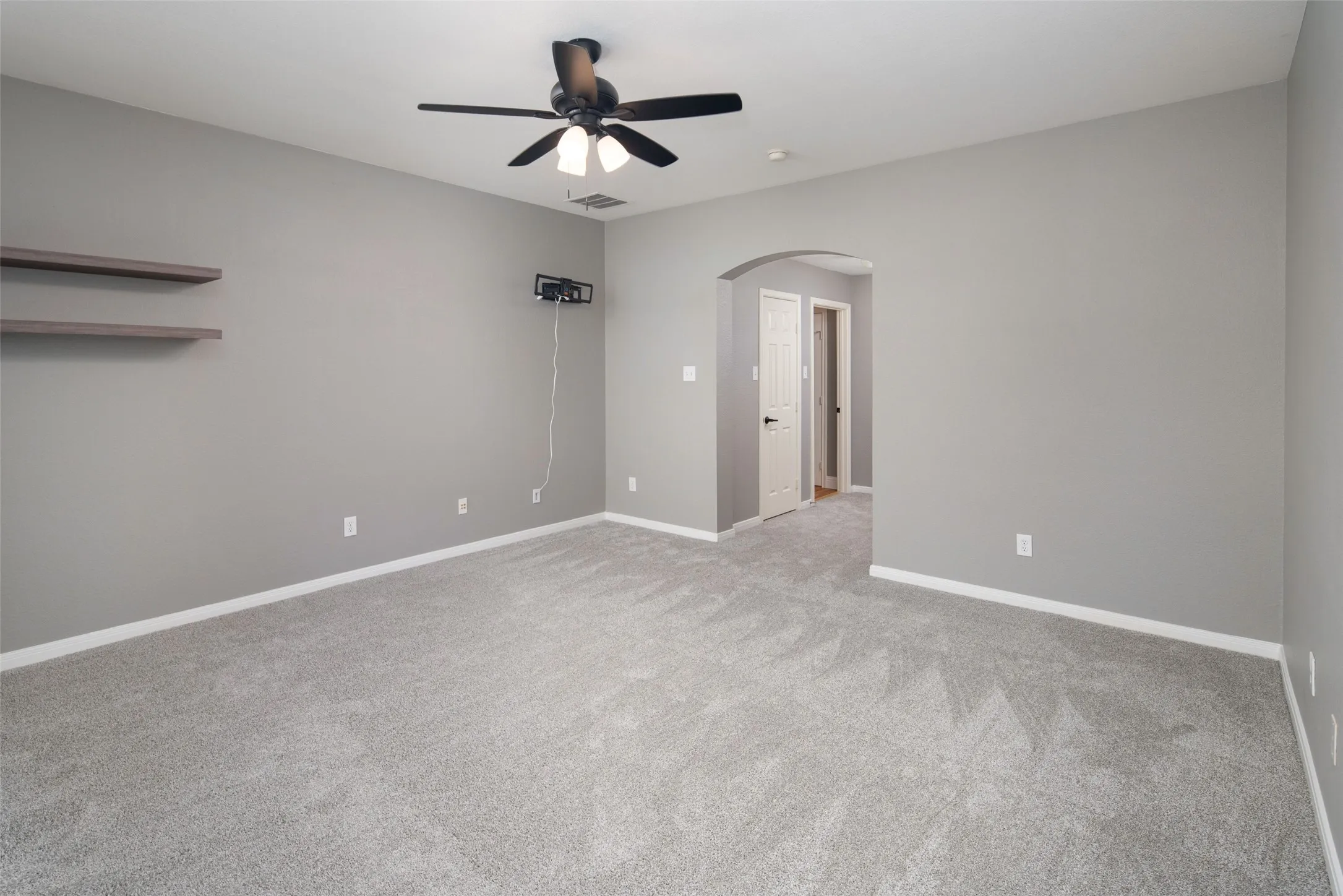 Spacious room featuring gray wall paint, light-colored patterned carpeting, white baseboards, and a ceiling fan with integrated lighting