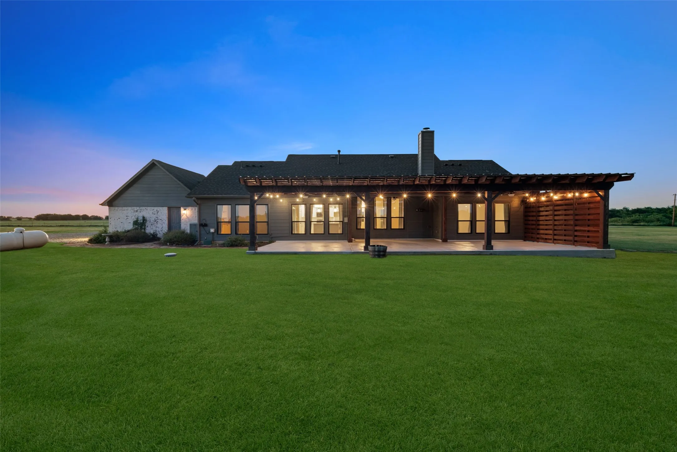 Expansive backyard featuring a manicured lawn, a large concrete patio, and a wood pergola with string lighting
