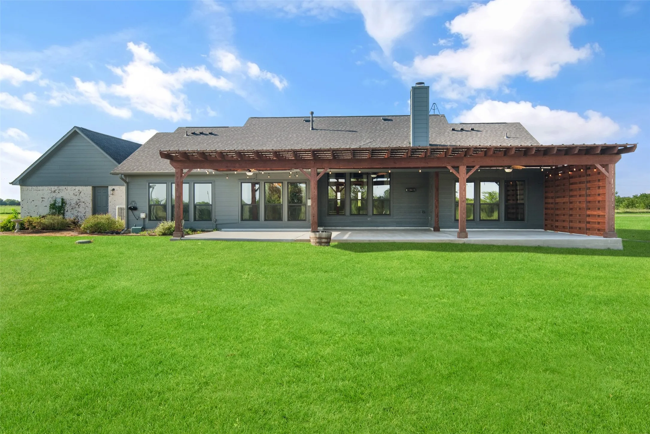 Expansive green lawn with a covered patio featuring a wood pergola and a privacy screen