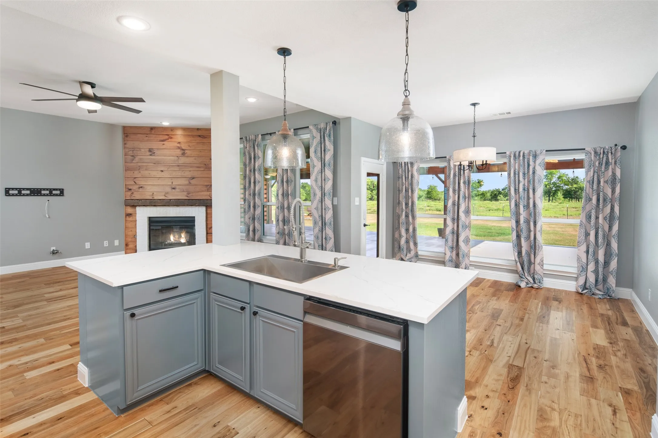Kitchen island featuring a stainless steel sink, integrated dishwasher, light-toned countertop, and pendant lighting