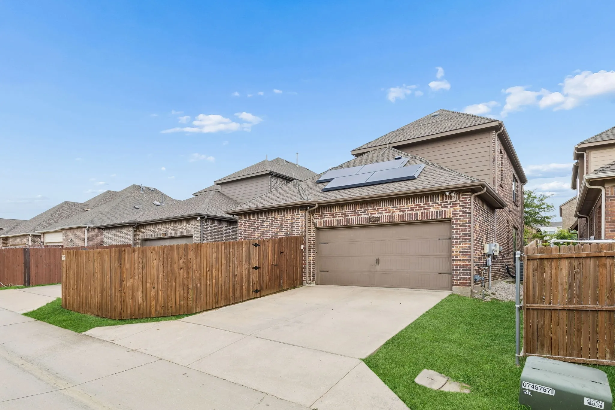 Brick exterior featuring an attached two-car garage, private wood fencing, solar panels, and a concrete driveway