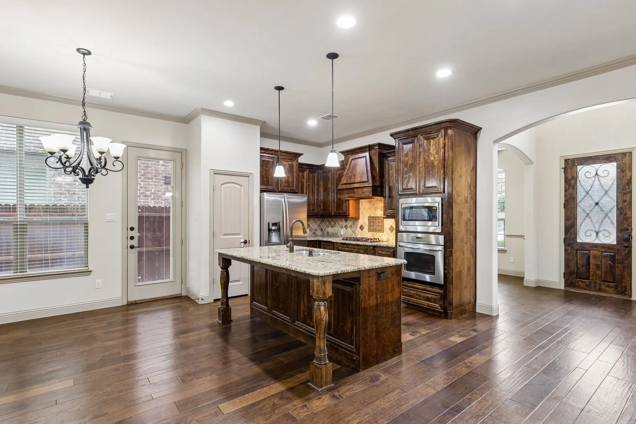 Gourmet kitchen featuring a central island with granite countertops, rich wood cabinetry, stainless steel appliances, and wood-finish flooring