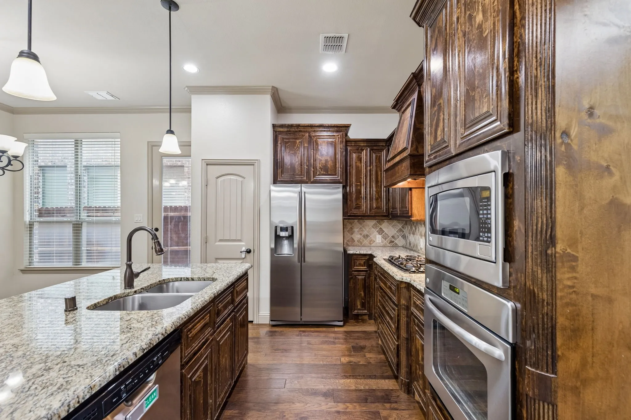Kitchen featuring wood-finish flooring, dark wood cabinetry, stainless steel appliances, granite countertops, and a double basin sink with a gooseneck faucet
