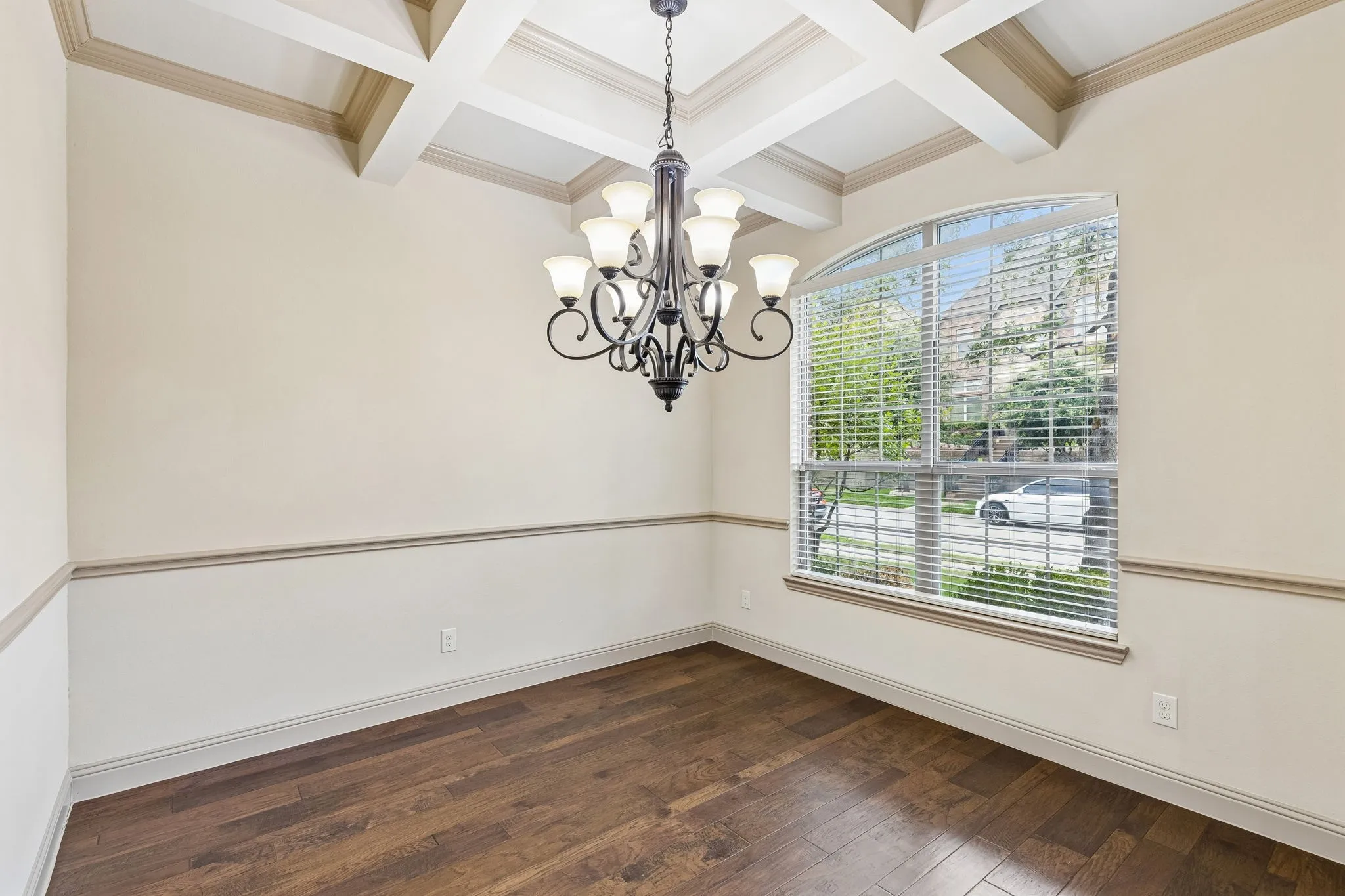 Room featuring coffered ceiling with a central chandelier, wood-finish flooring, and a large arched window