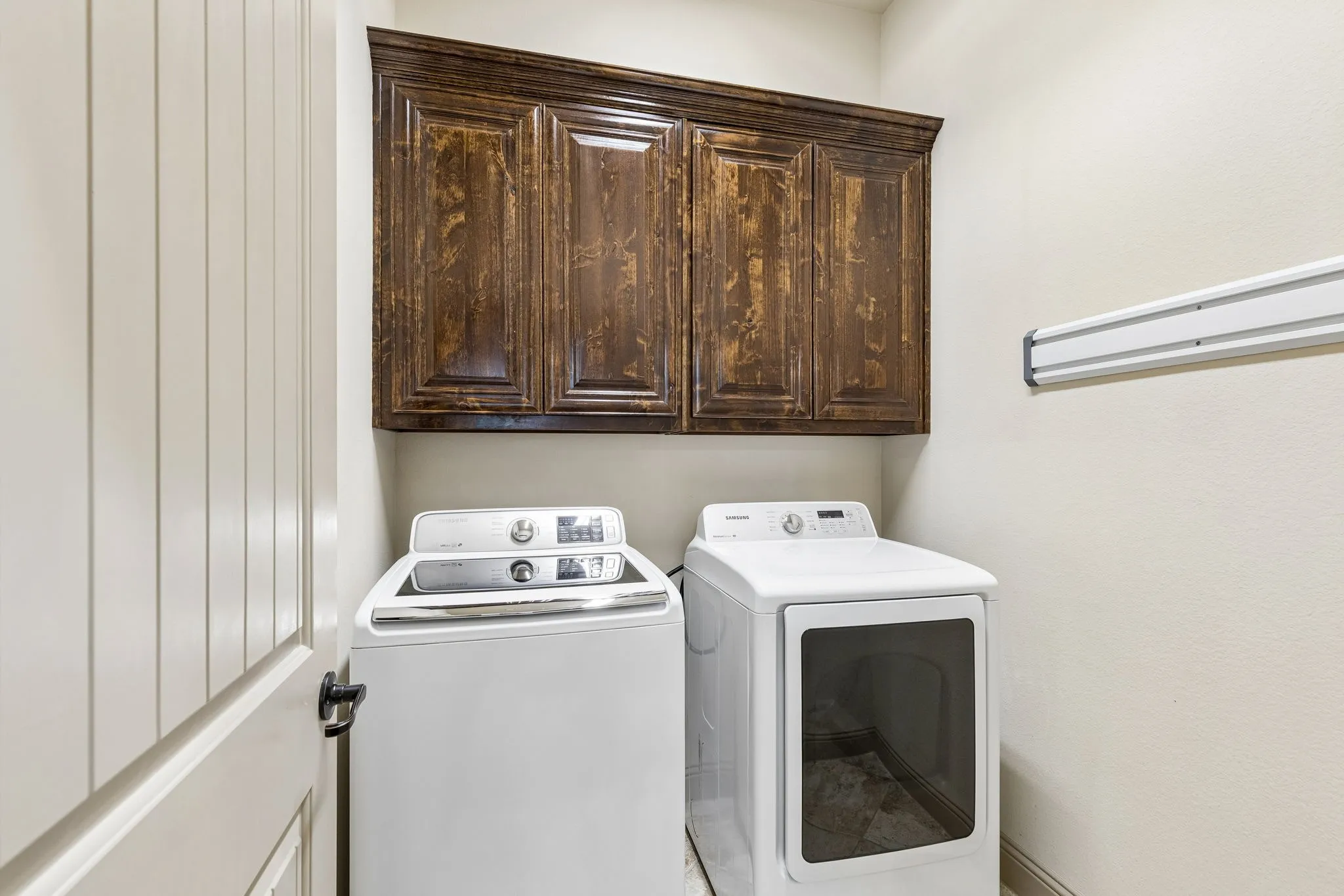 Dark wood-finish cabinetry provides storage above a dedicated laundry area with white walls and a light-colored door featuring vertical paneling