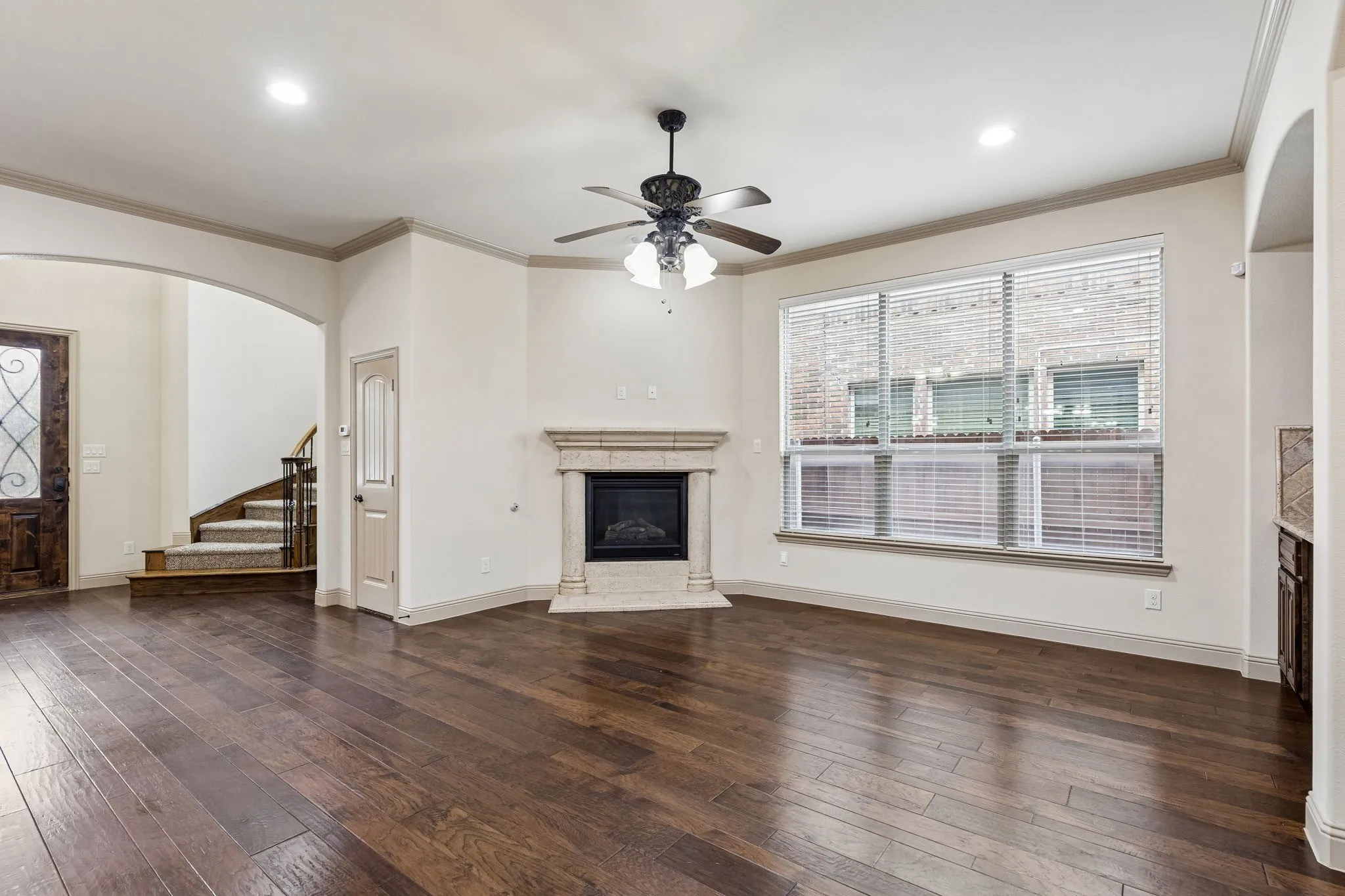 Spacious living area featuring dark wood-finish flooring, a corner fireplace with a light-colored stone surround, multiple large windows, recessed lighting, and a ceiling fan