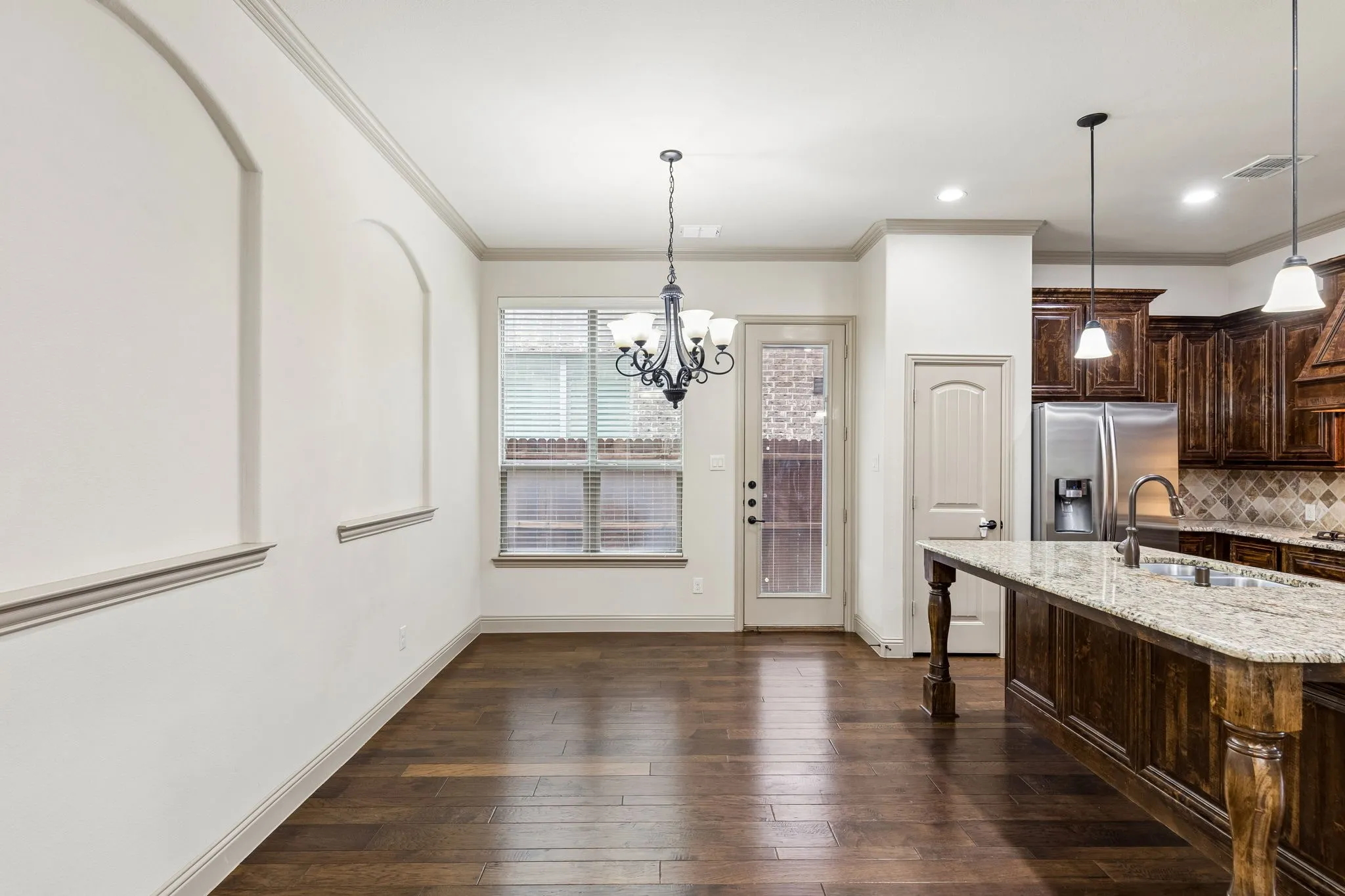Open-concept dining area with wood-finish flooring, crown molding, and decorative wall arches
