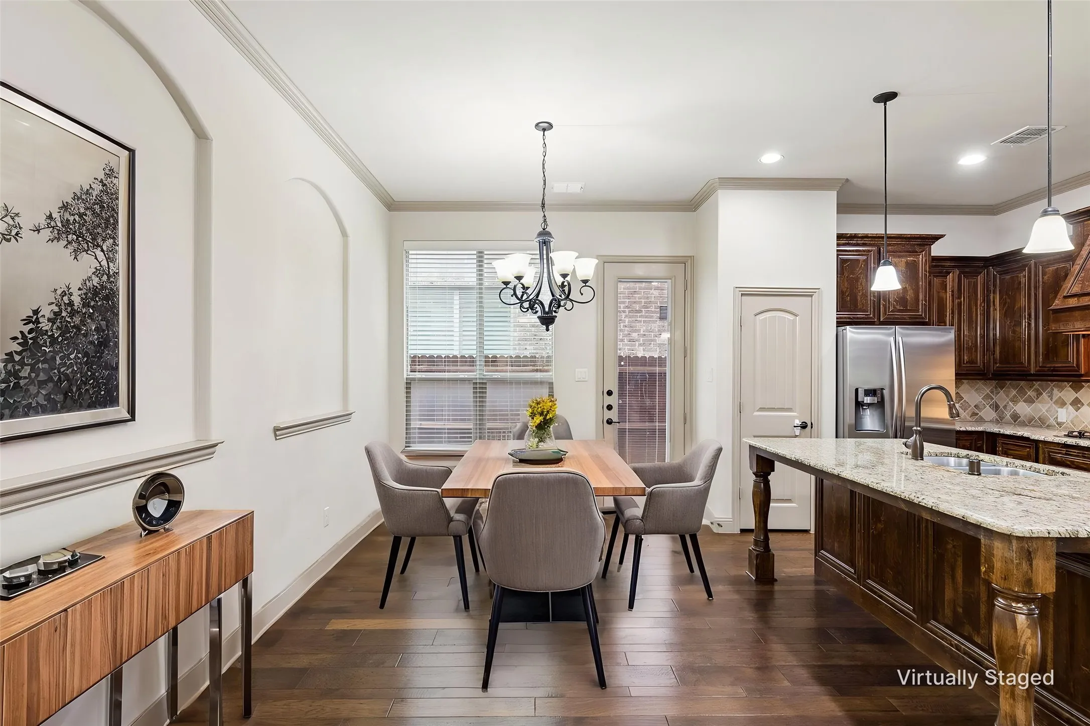 Open-concept dining area featuring wood-finish flooring, crown molding, and an arched wall niche