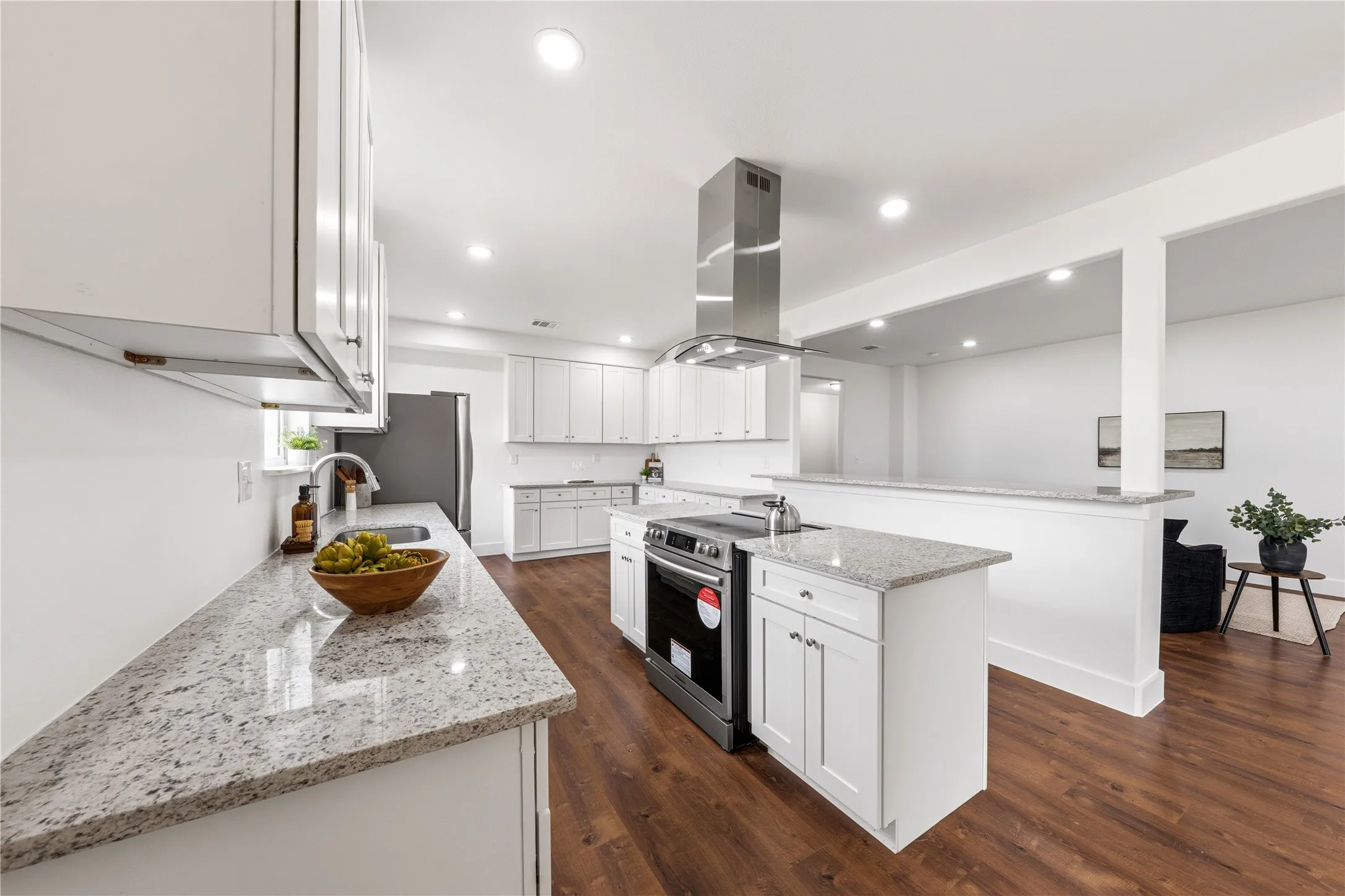 Modern kitchen featuring white cabinetry, light-toned countertops, a stainless steel range hood, and wood-finish flooring